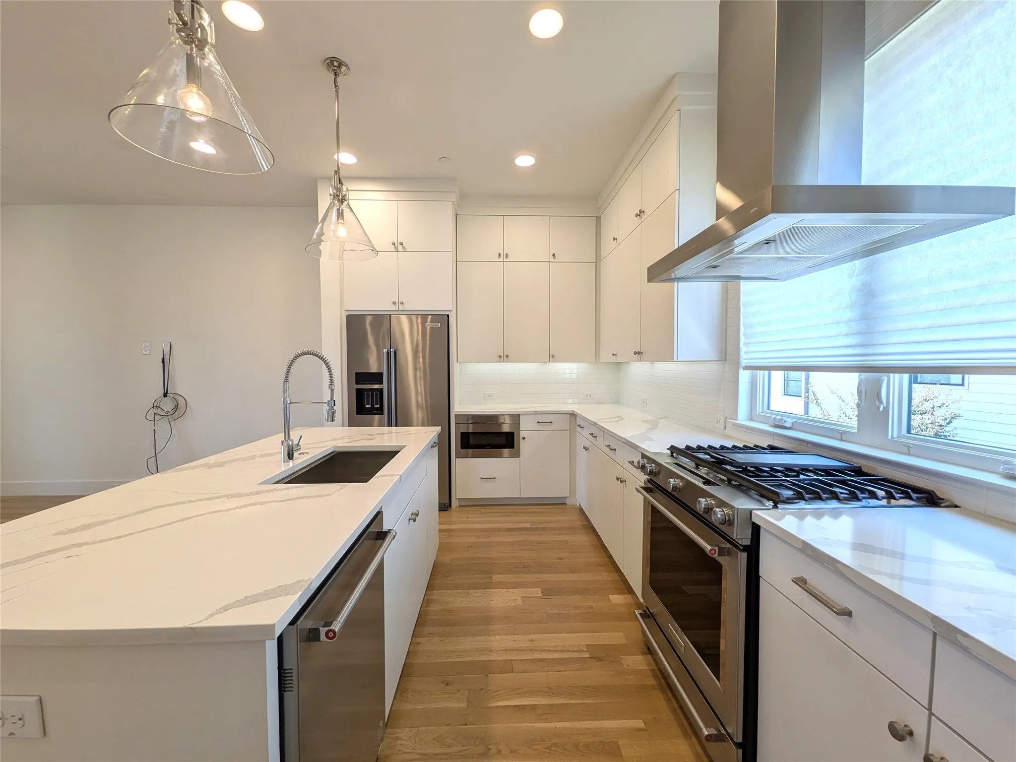Kitchen featuring white cabinetry, light wood-finish flooring, stainless steel appliances, a center island with sink, and white countertops