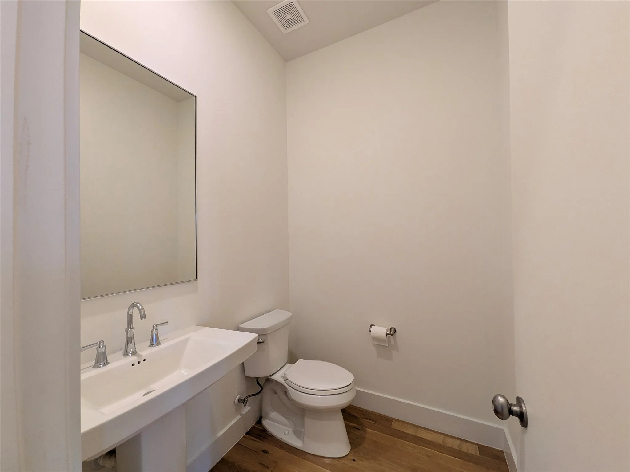 Modern pedestal sink with polished chrome fixtures, rectangular mirror, and wood-finish flooring