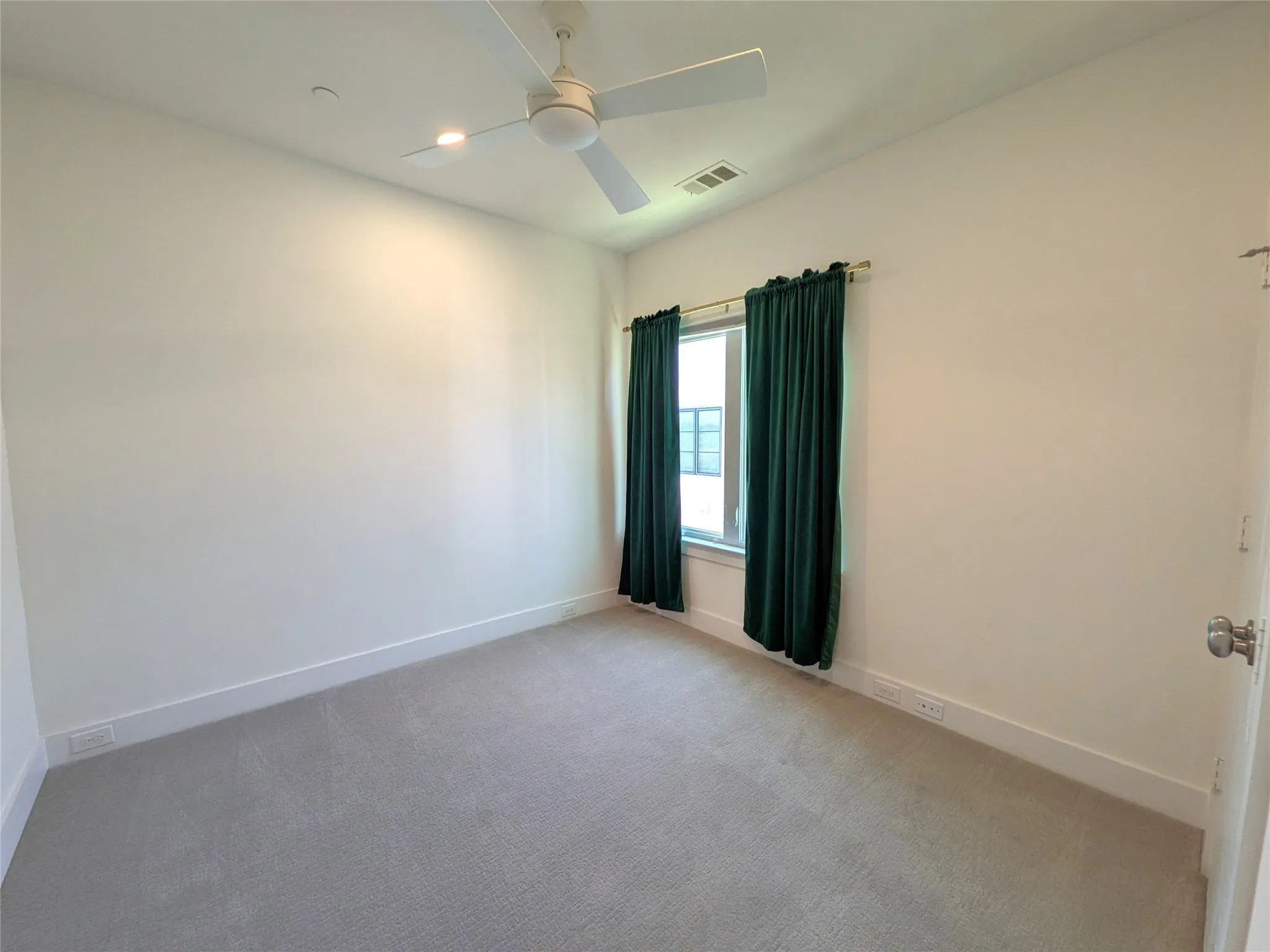Wall-to-wall carpet flooring, integrated ceiling fan with lighting, ample wall space, and window with curtain rod