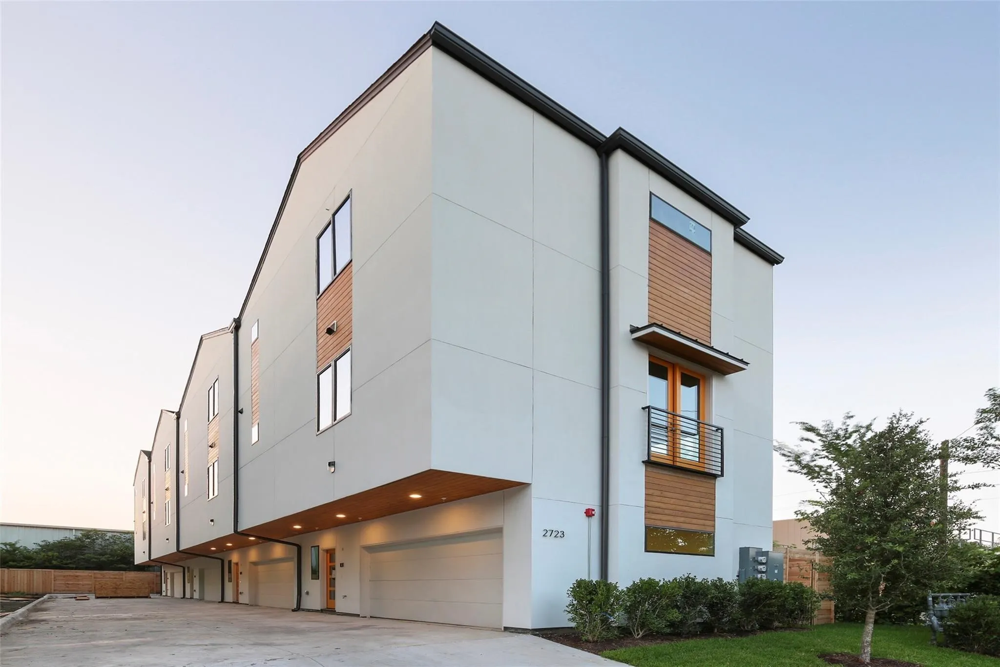 Contemporary architectural design featuring a white facade, wood-finish accents, multiple windows, and an attached garage