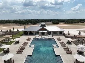Resort-style pool with integrated steps, surrounding concrete deck, and adjacent clubhouse with a metal roof