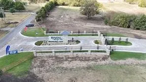 Community entrance featuring a stone perimeter fence, landscaped median, and paved roadways