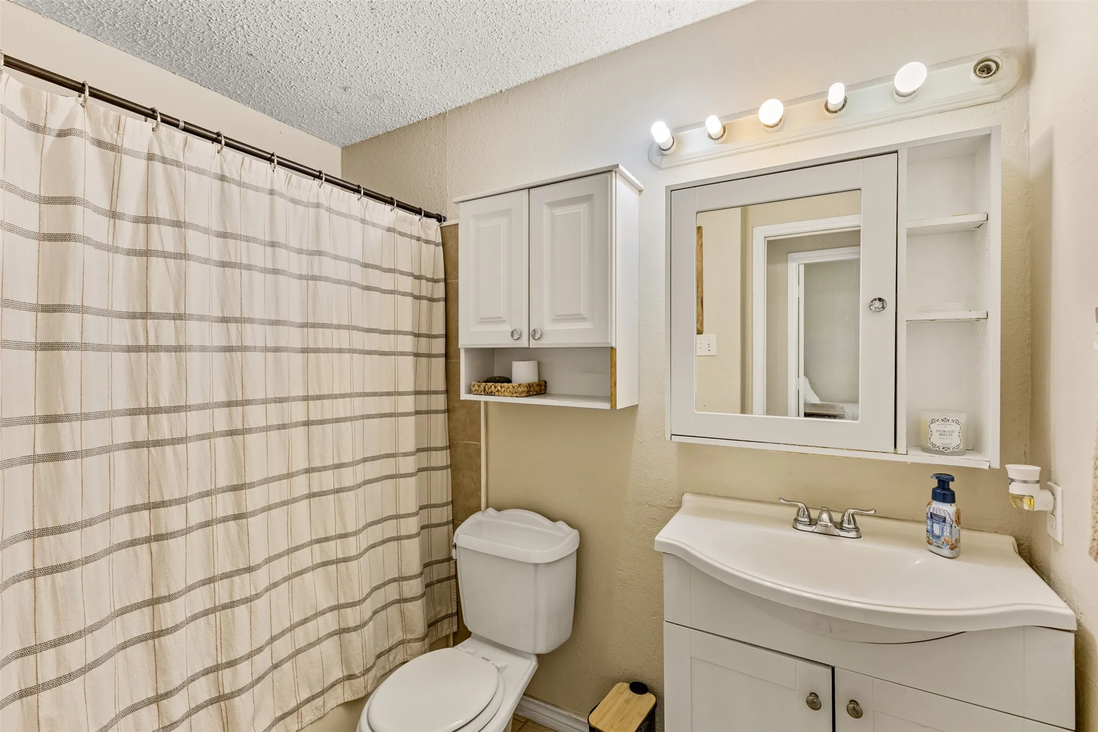 Vanity with an integrated sink and base cabinetry, a medicine cabinet with open shelving, and a wall-mounted light fixture