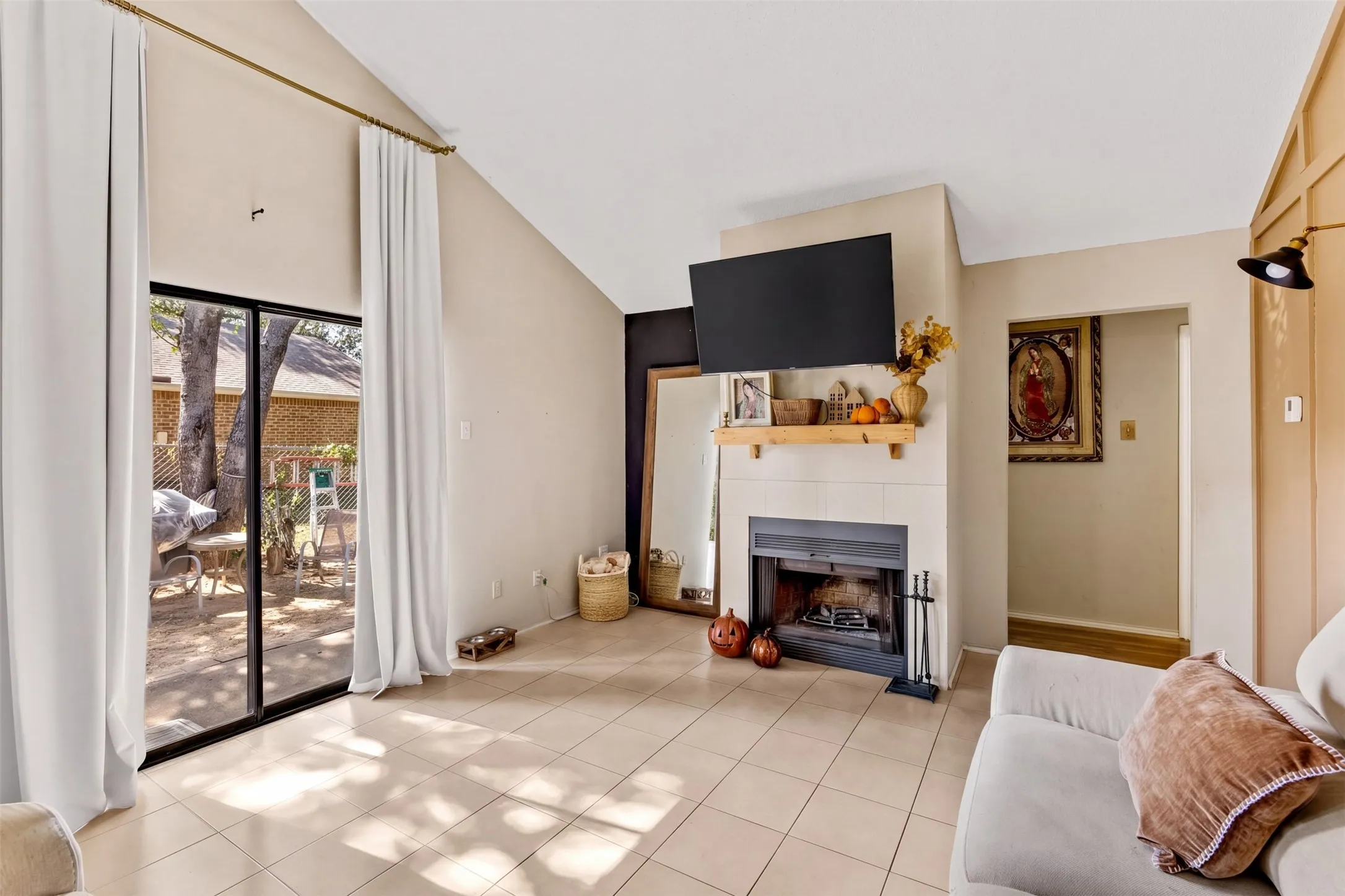 Vaulted ceilings, a built-in fireplace, tile flooring, and a sliding glass door providing outdoor access