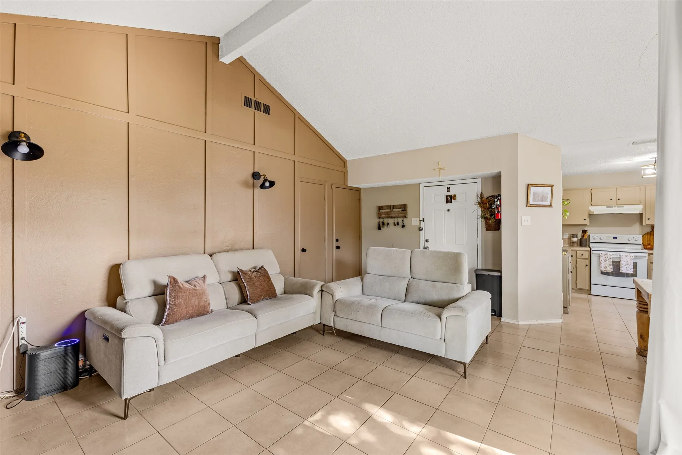 Vaulted ceiling with exposed beam, panel accent wall, tile flooring, and integrated wall sconces