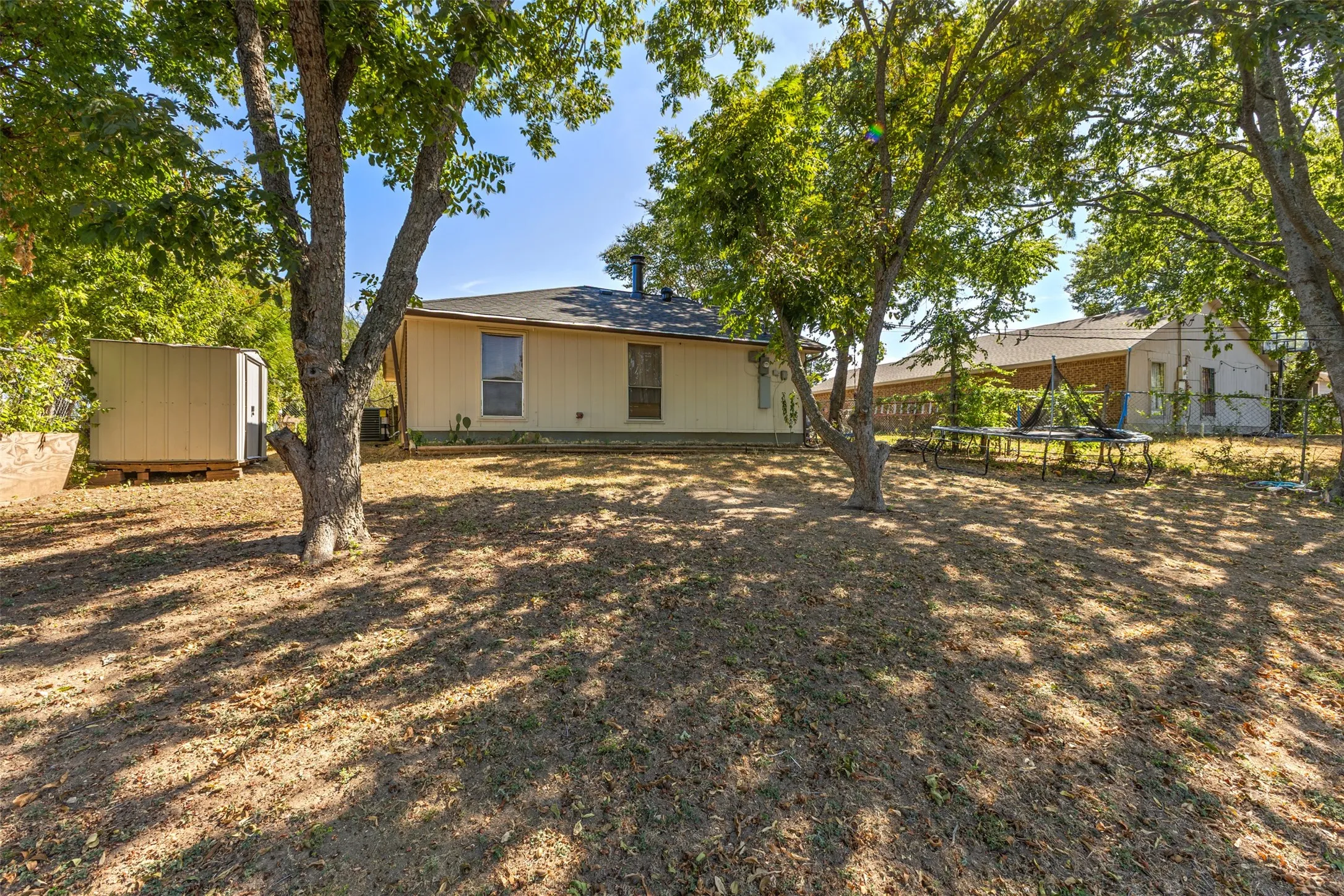 Expansive rear yard featuring mature trees, a detached storage shed, and a single-story residence with a shingled roof