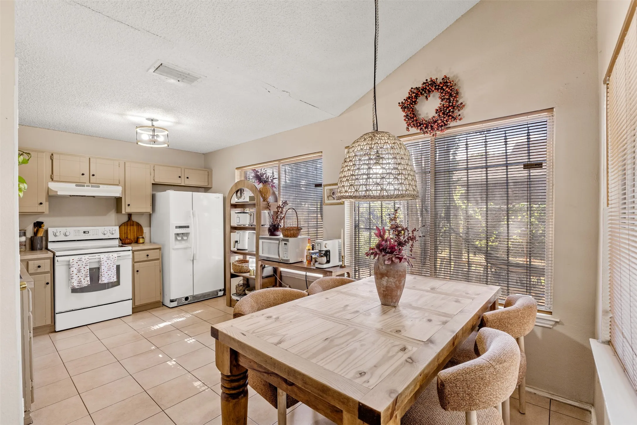 Kitchen and dining area featuring vaulted ceilings, light-toned cabinetry, tile flooring, and a window with blinds