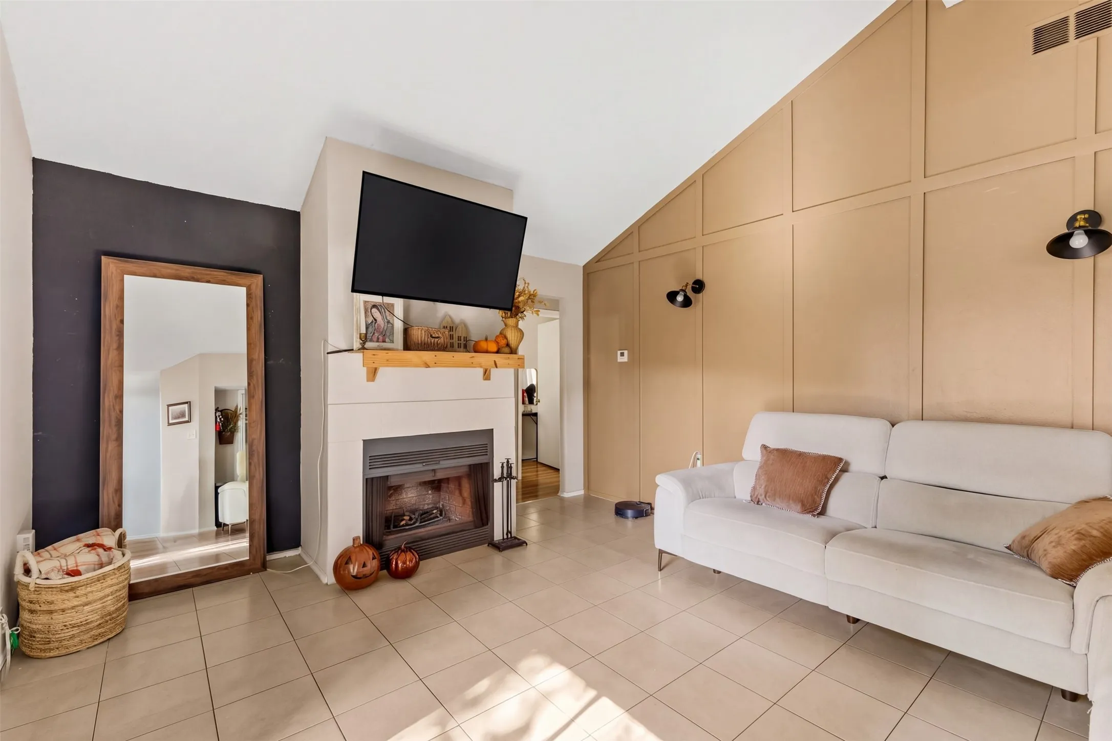 Vaulted ceiling, built-in fireplace, wood mantel, tile flooring, and accent wall paneling