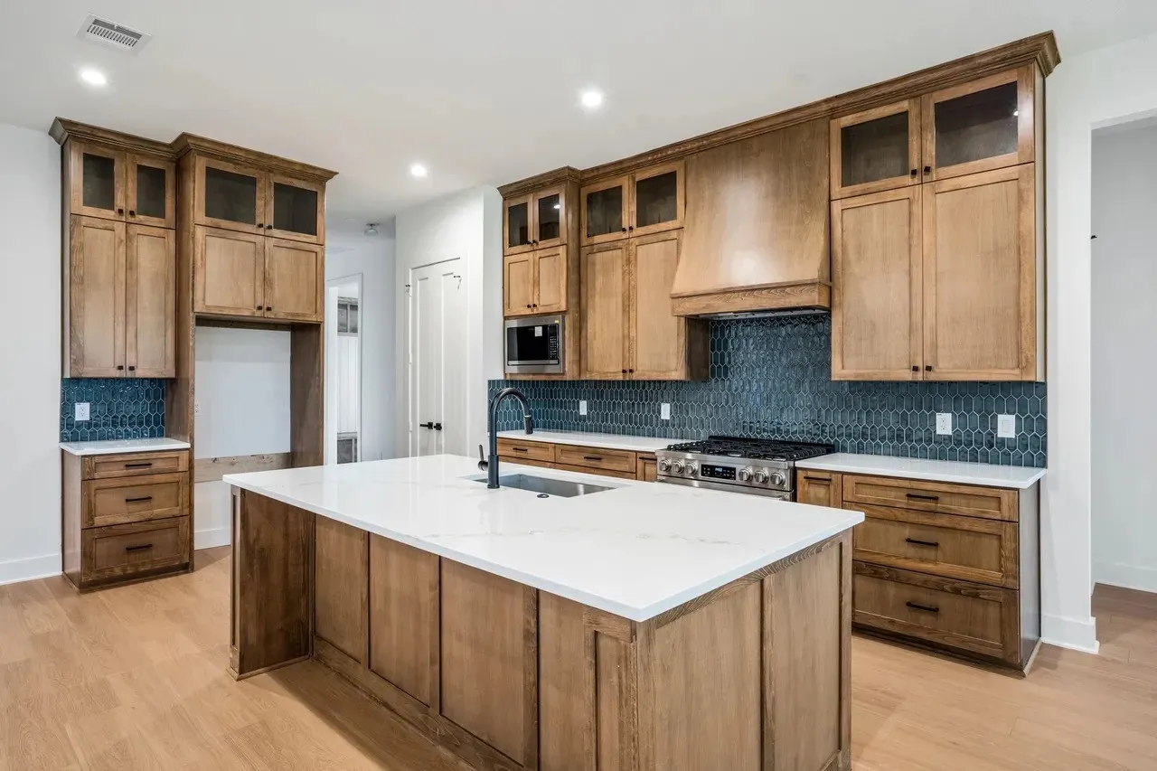 Kitchen featuring a large central island with a white countertop, wood-finish cabinetry, a stainless steel range, and a blue geometric tile backsplash
