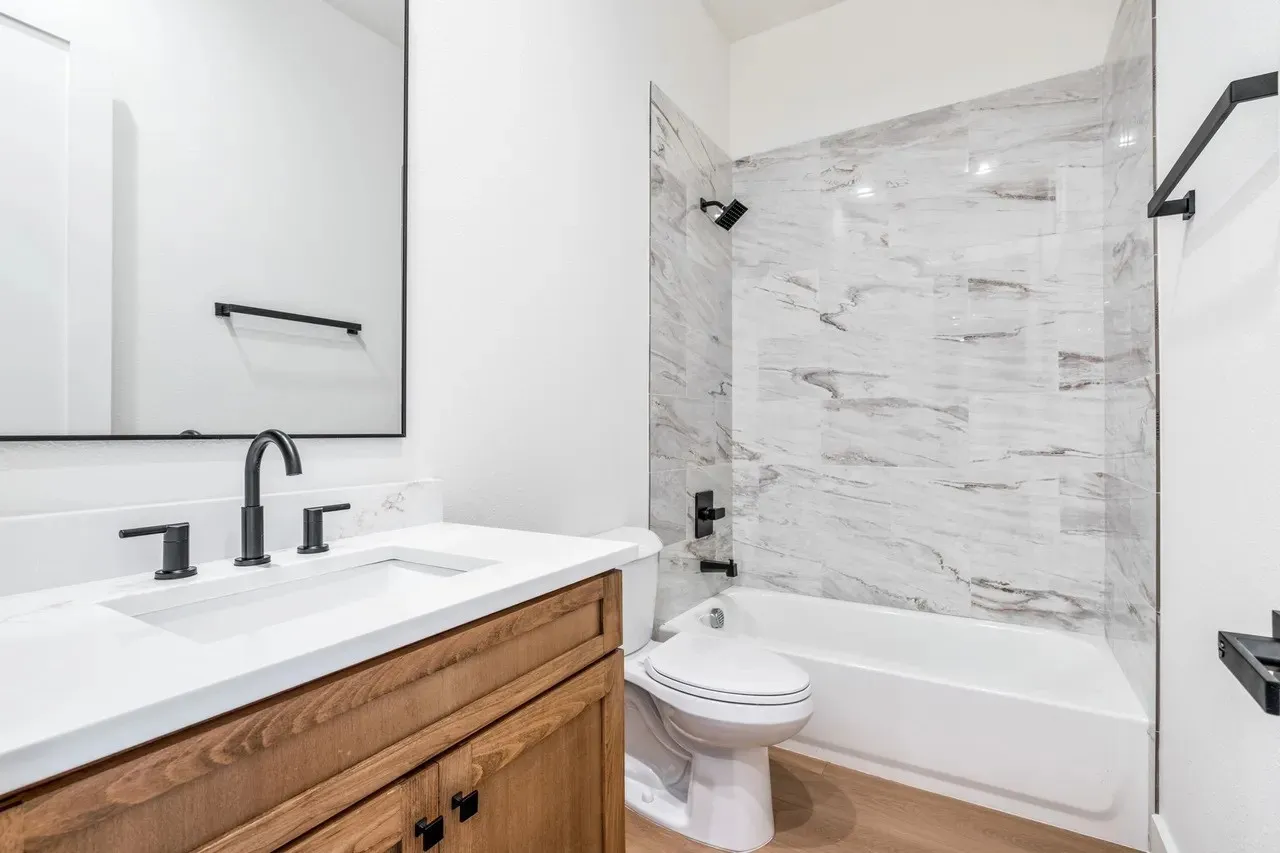 White countertop with an integrated sink, wood-finish vanity, and matte black fixtures
