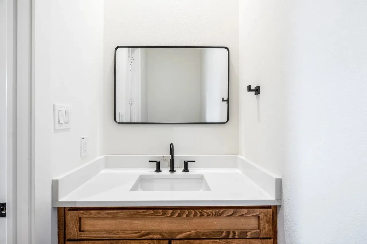 Custom wood vanity with a white solid surface countertop, undermount sink, and matte black fixtures
