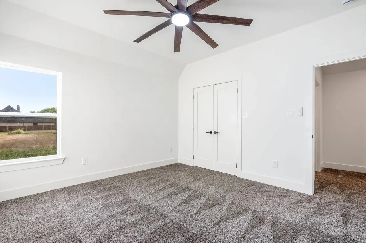 Vaulted ceiling with a contemporary ceiling fan, white walls, and a window offering natural light