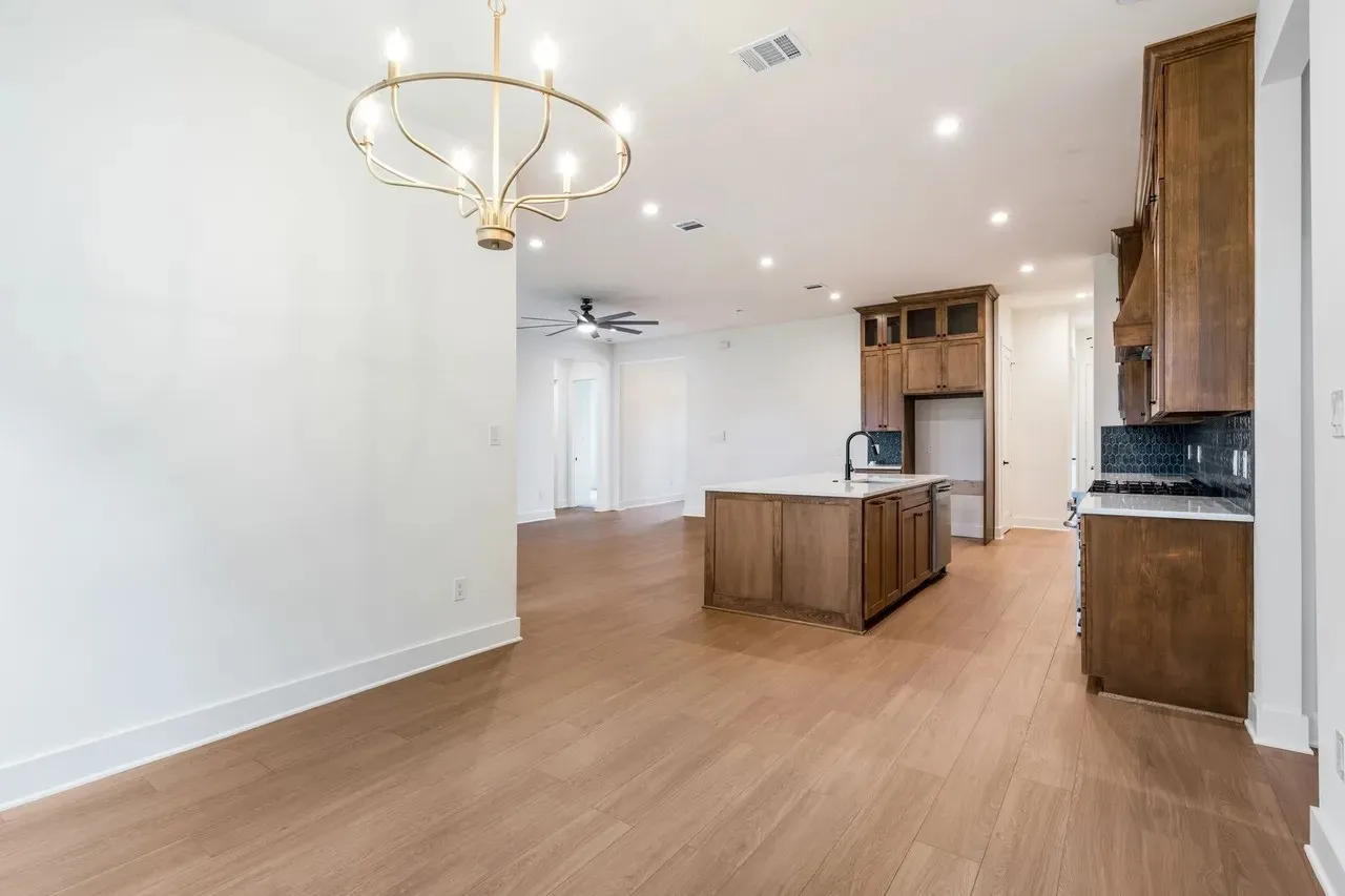 Wood-finish flooring, recessed lighting, kitchen island with sink and white countertop, dark wood cabinetry, and a dark tile backsplash