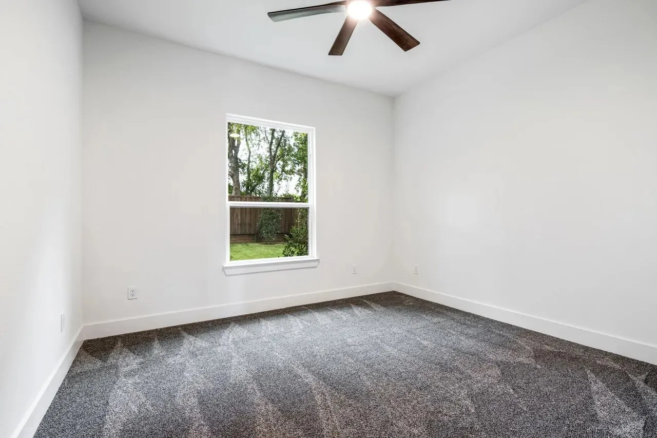 Neutral wall color, textured carpeting, contemporary ceiling fan with light, single window with exterior greenery