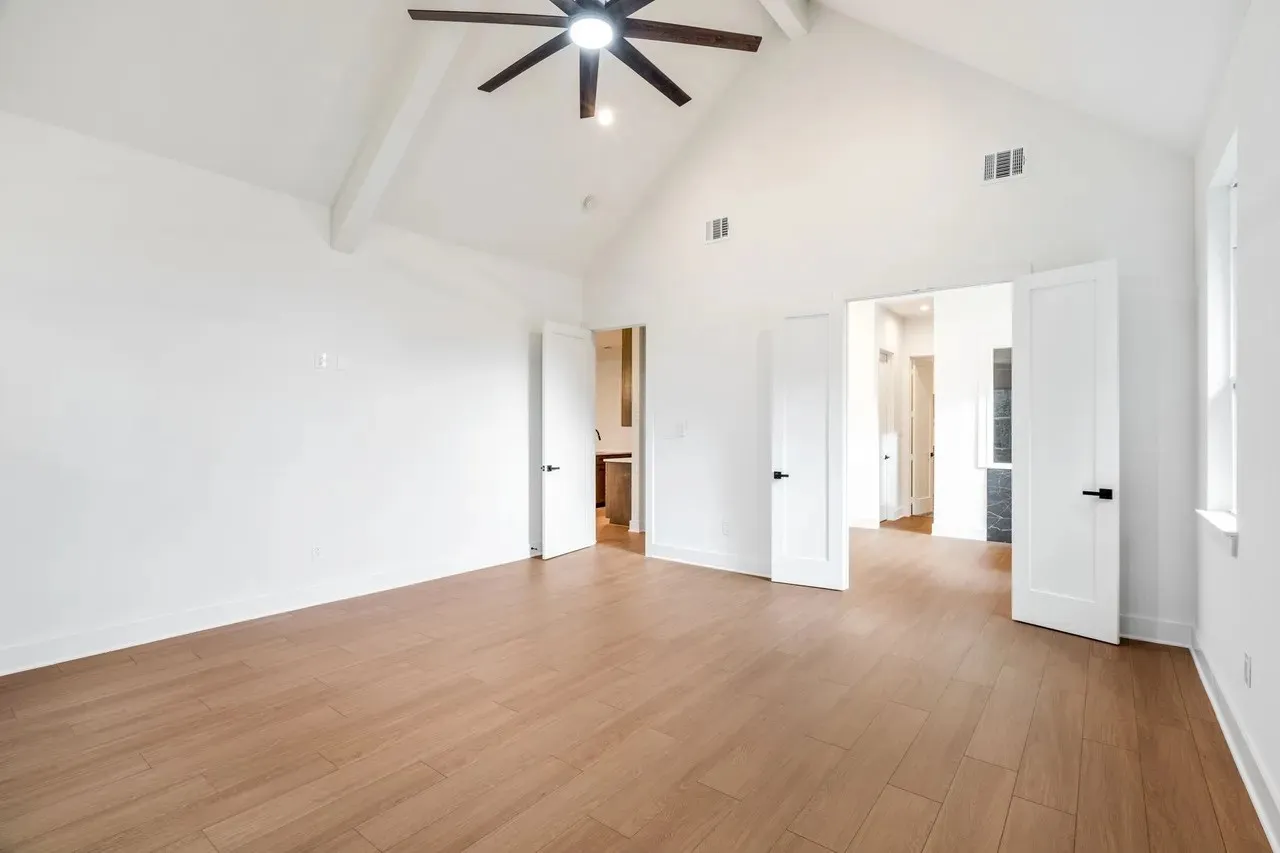 Vaulted ceiling with exposed beam, wood-finish flooring, ceiling fan, and double panel doors with matte black hardware