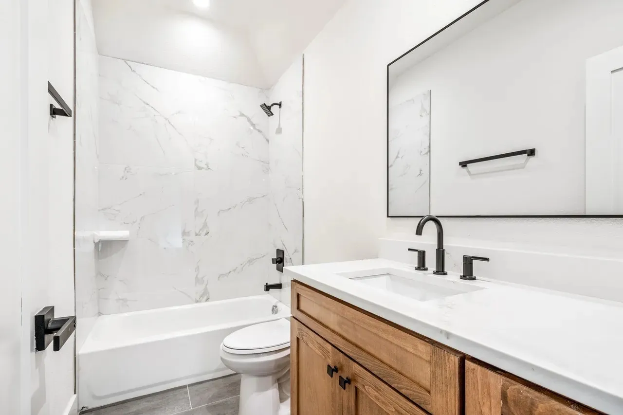 White vanity with a wood-finish base, integrated sink, and matte black fixtures