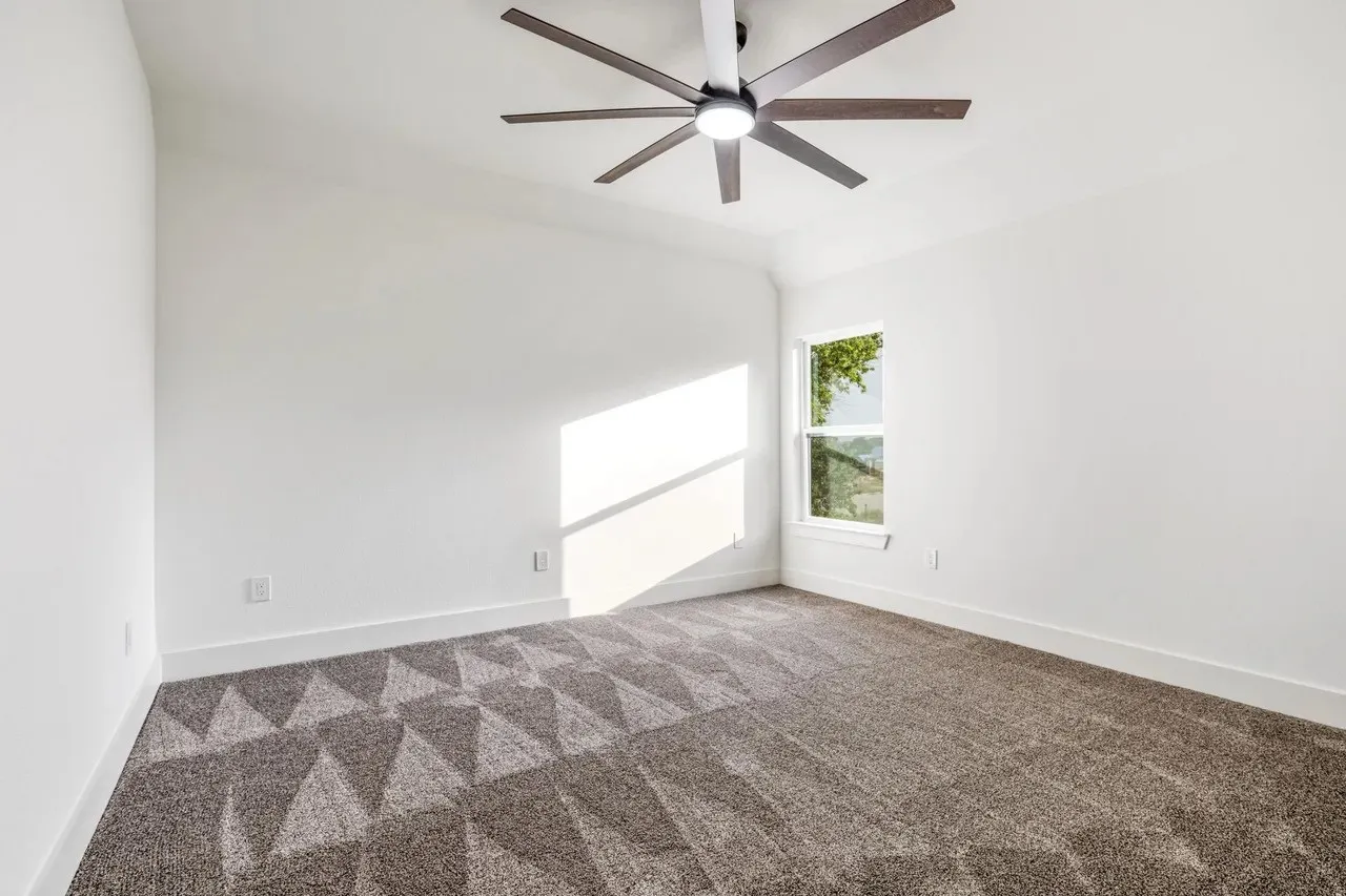 Bright room featuring a contemporary ceiling fan, white walls, and geometric pattern carpeting
