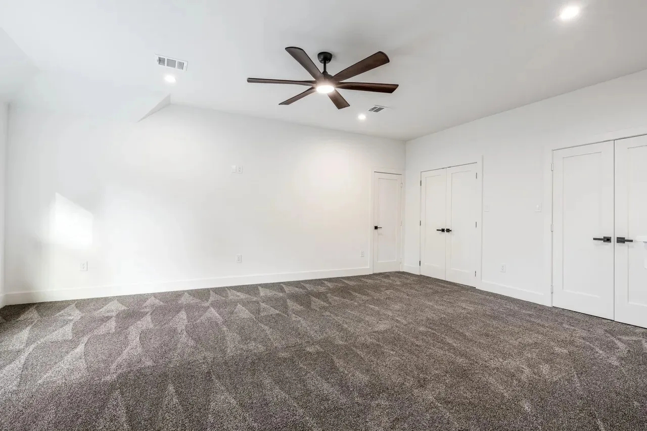 Spacious room featuring patterned carpeting, a dark-toned ceiling fan, recessed lighting, and multiple white panel doors with matte black hardware