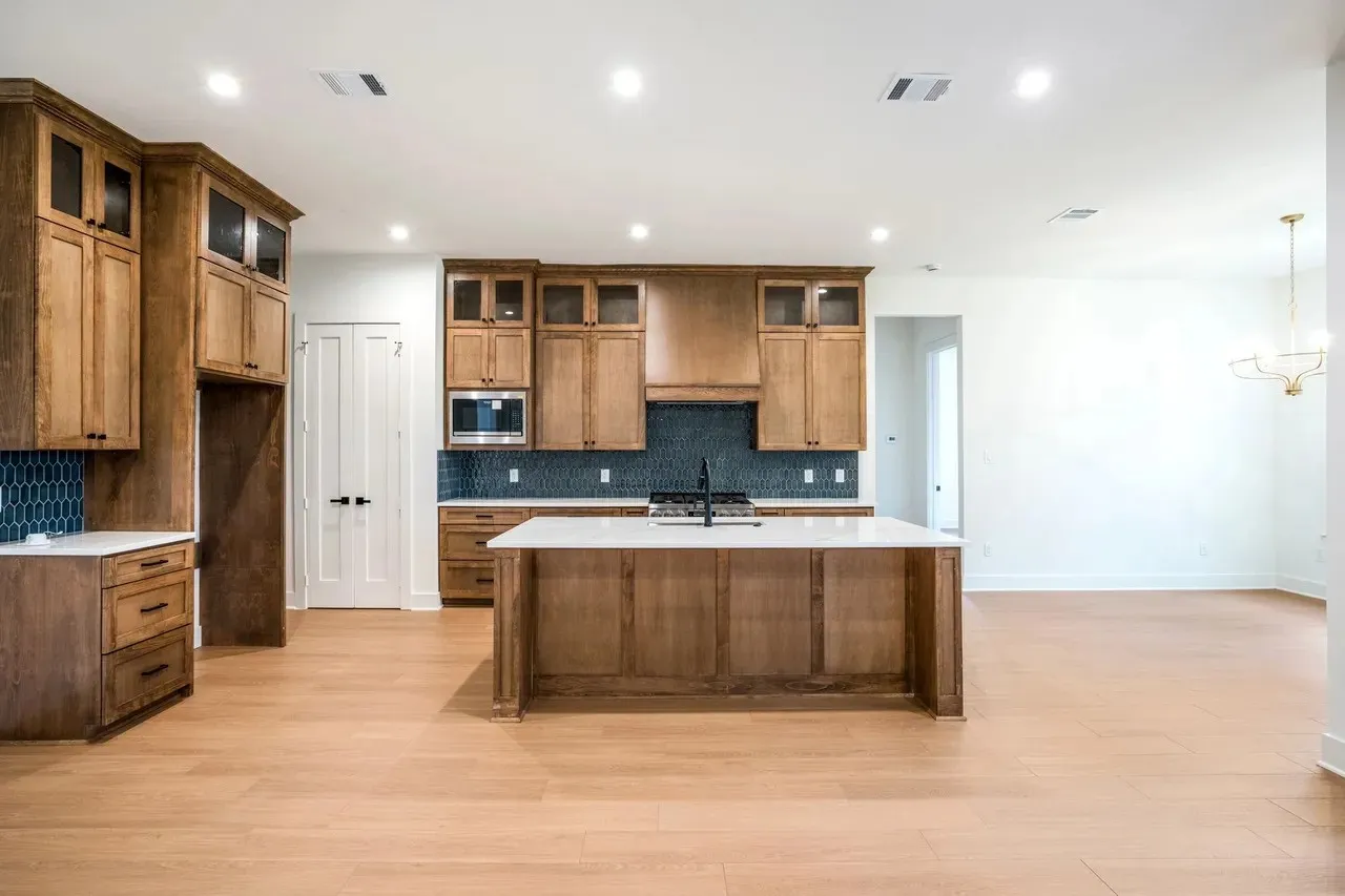 Kitchen featuring wood cabinetry, white countertops, tile backsplash, stainless steel microwave, and wood-finish flooring