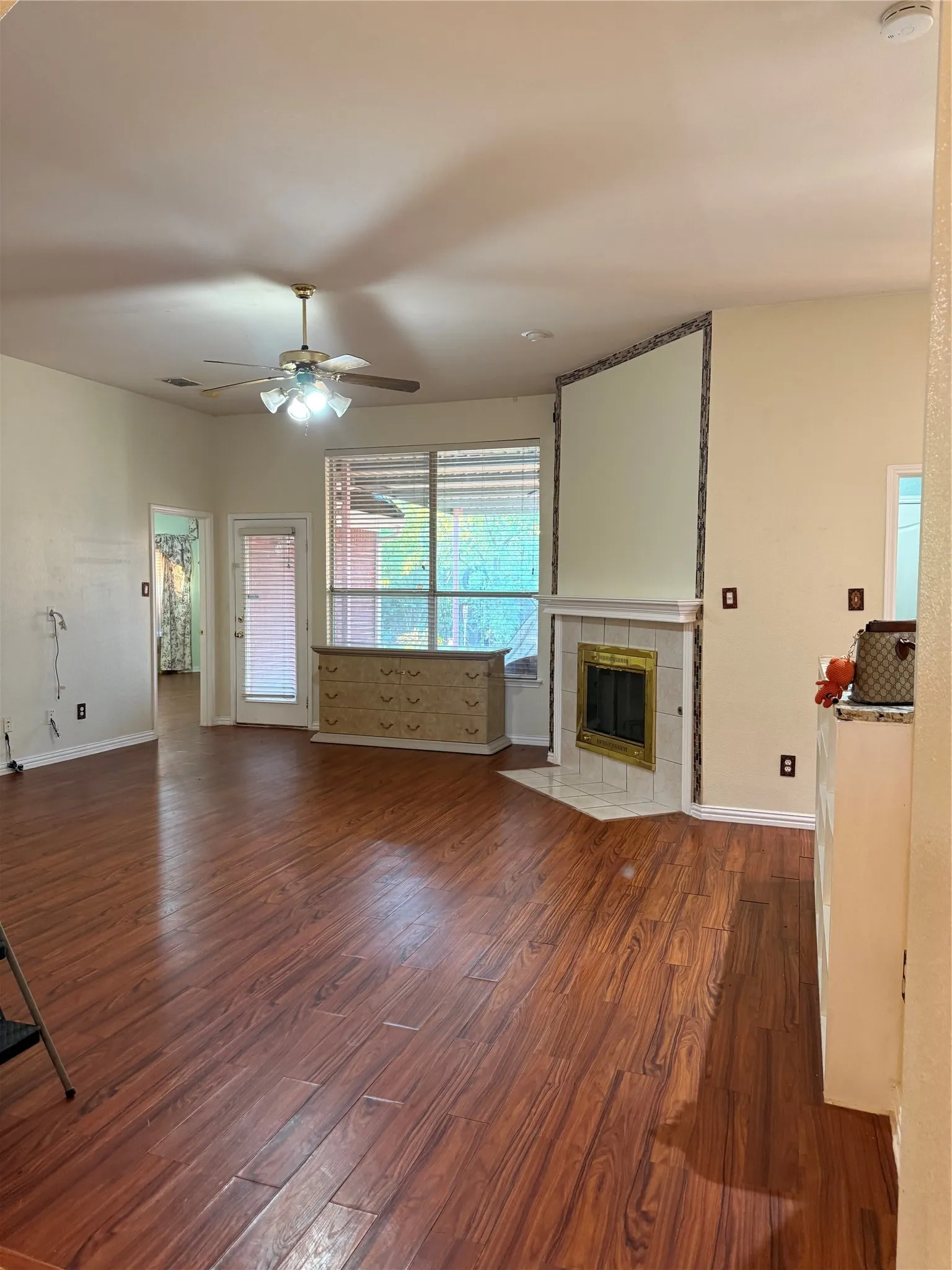 Wood-finish flooring throughout, corner fireplace with tile surround, ceiling fan with integrated lighting, expansive windows, and a built-in cabinetry unit