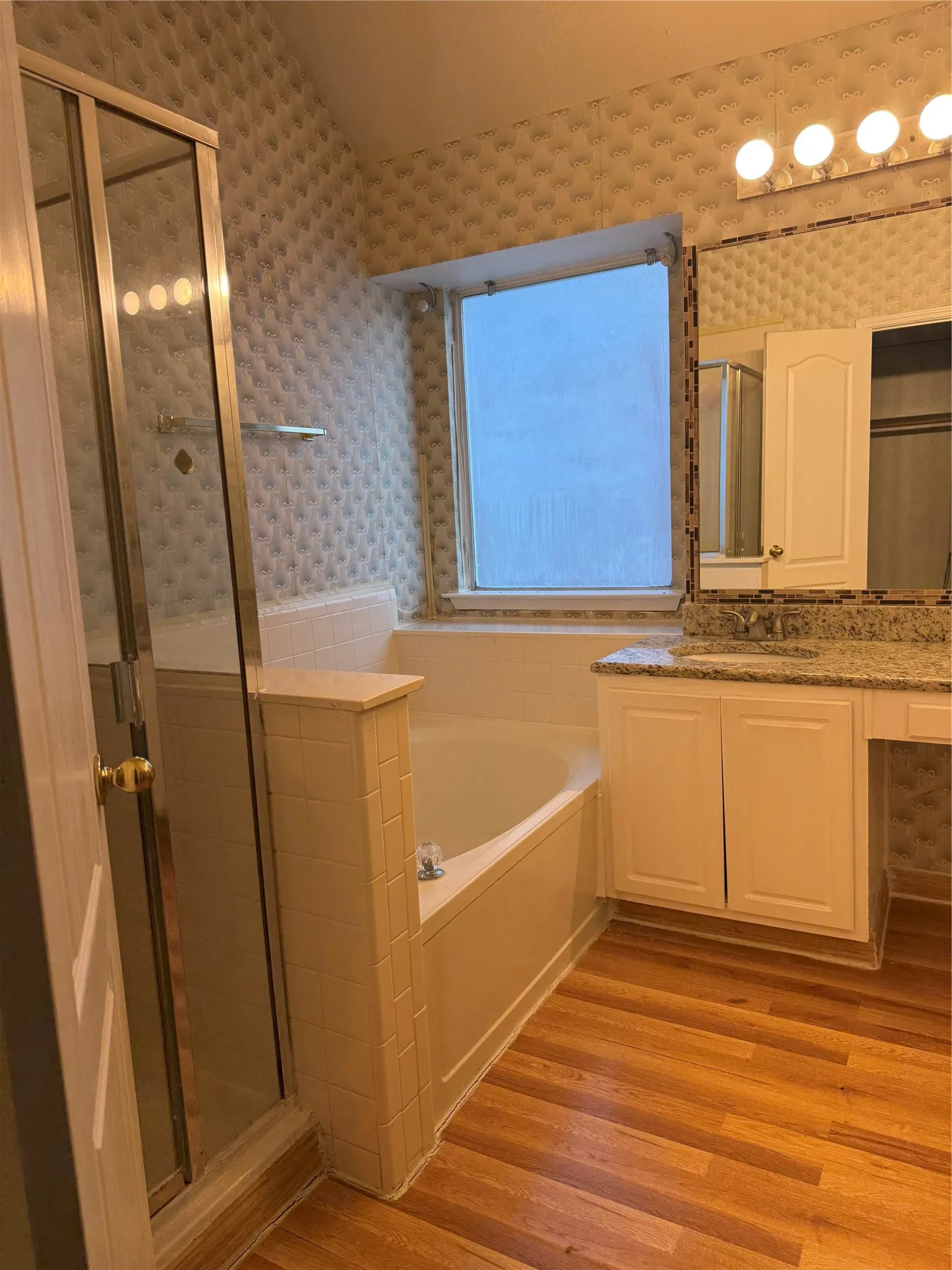 Enclosed glass shower, built-in soaking tub, wood-finish flooring, vanity with integrated sink, and overhead lighting fixture