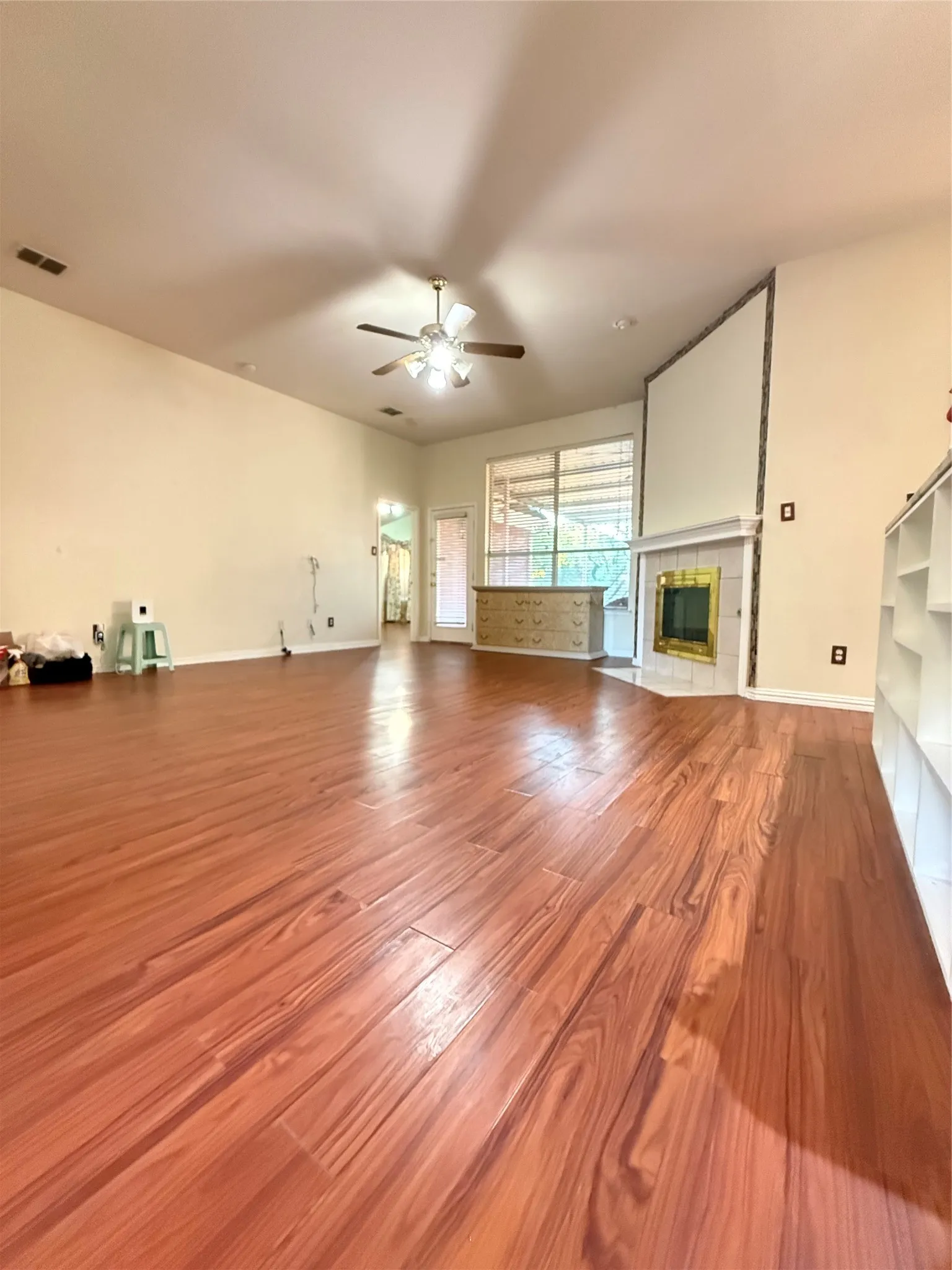 Vaulted ceilings, wood-finish flooring, a ceiling fan, a fireplace with a decorative surround, and built-in shelving