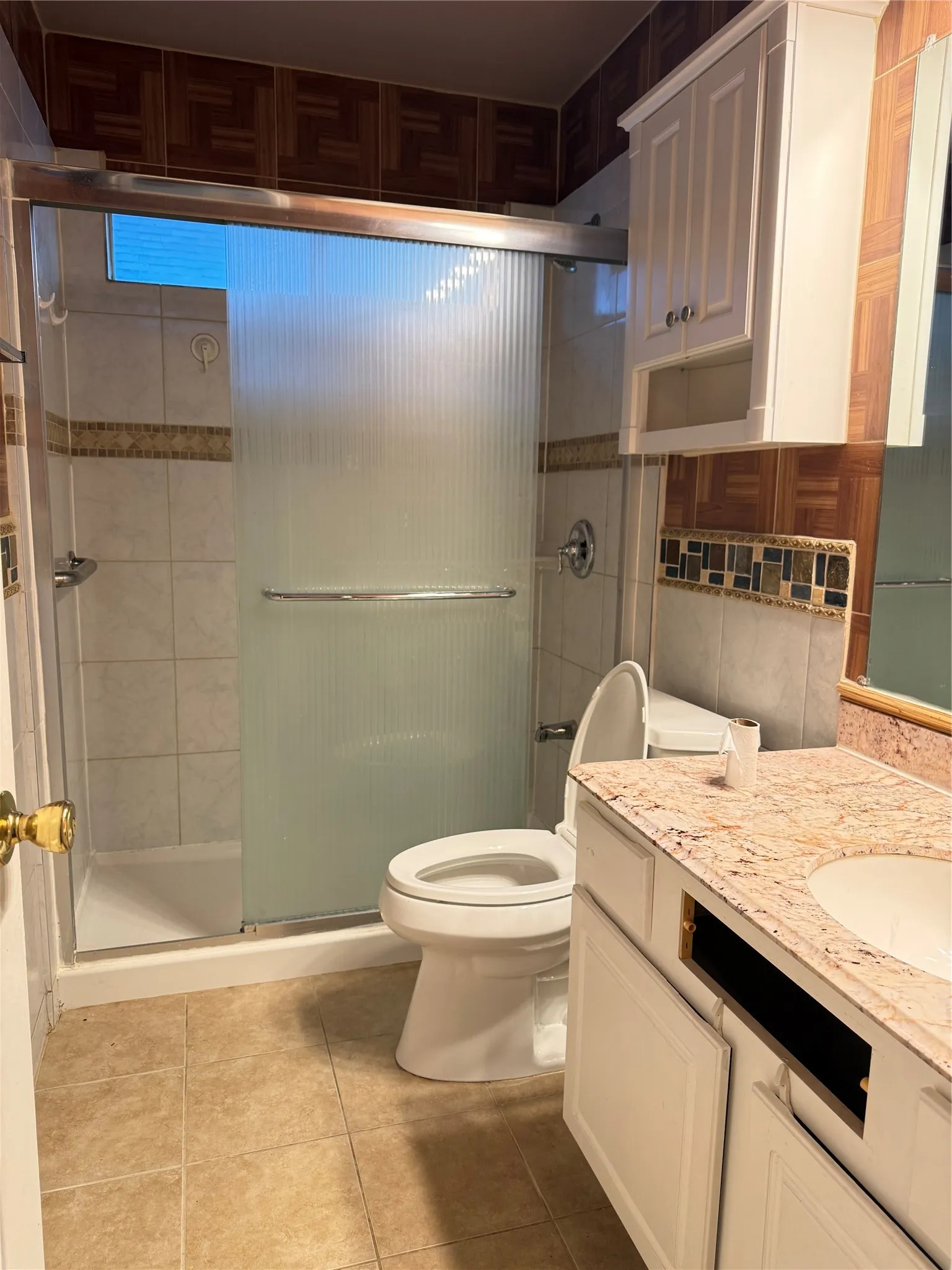 Walk-in shower with frosted glass enclosure, single vanity with integrated sink, stone-finish countertop, white cabinetry, and floor tiling
