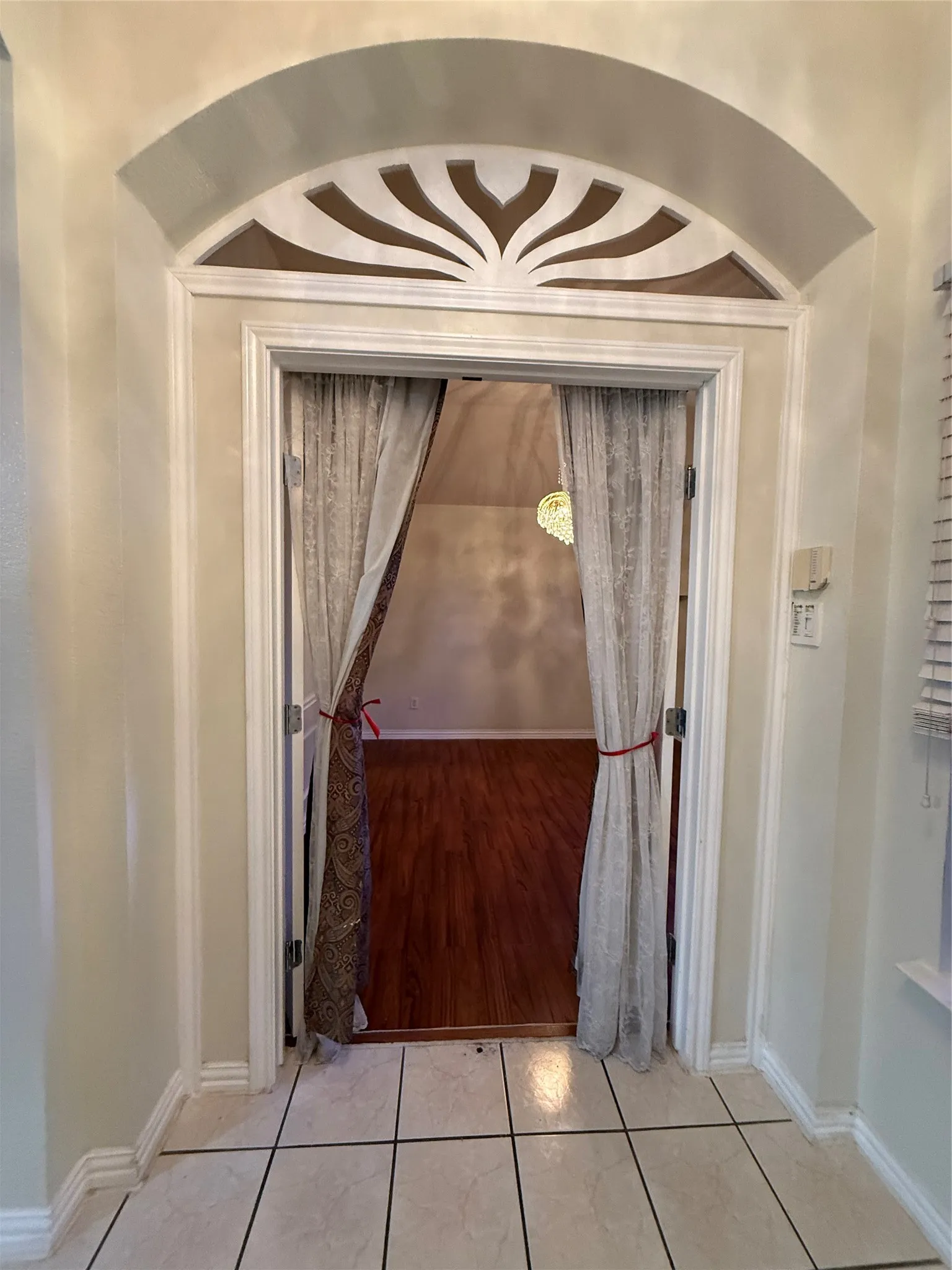Arched entryway with decorative transom, tiled flooring, and wood-finish flooring beyond