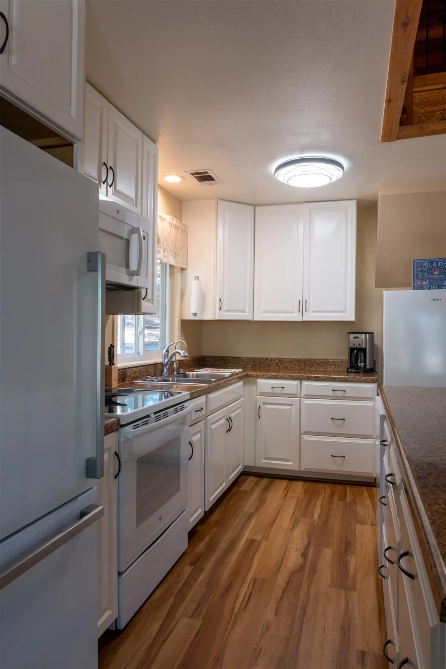 White cabinetry, wood-finish flooring, stainless steel refrigerator, white electric range, and laminate countertops