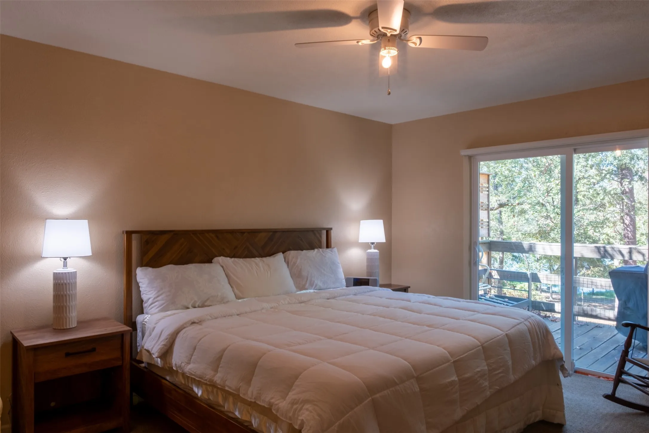 Wood headboard, ceiling fan, sliding glass door, and exterior deck