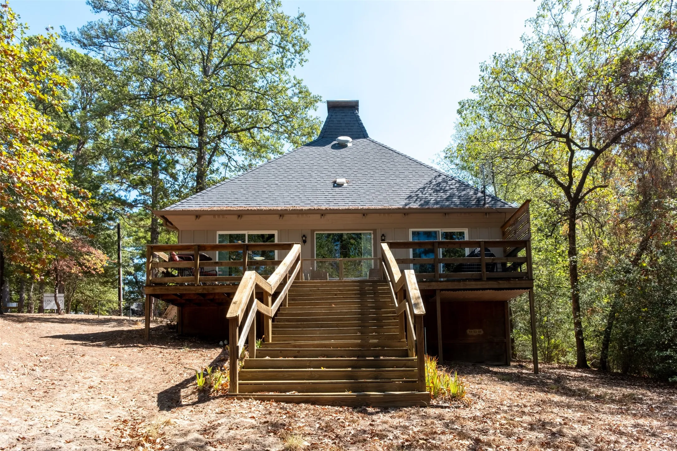 Gabled roofline residence featuring a prominent wooden staircase, expansive elevated deck, and a distinctive chimney design
