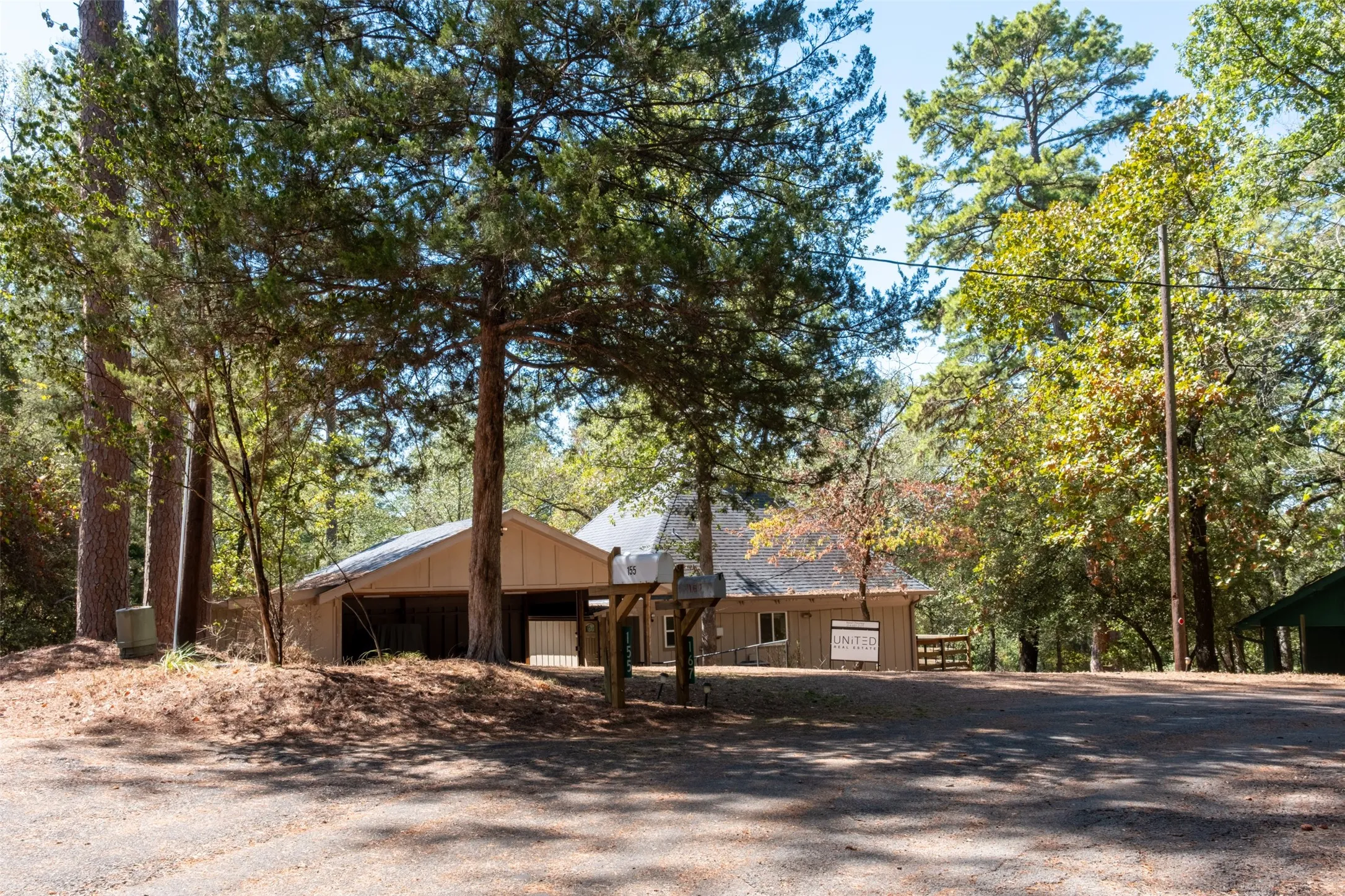 Wood-sided residence with a covered carport and a sloped roofline, surrounded by mature trees