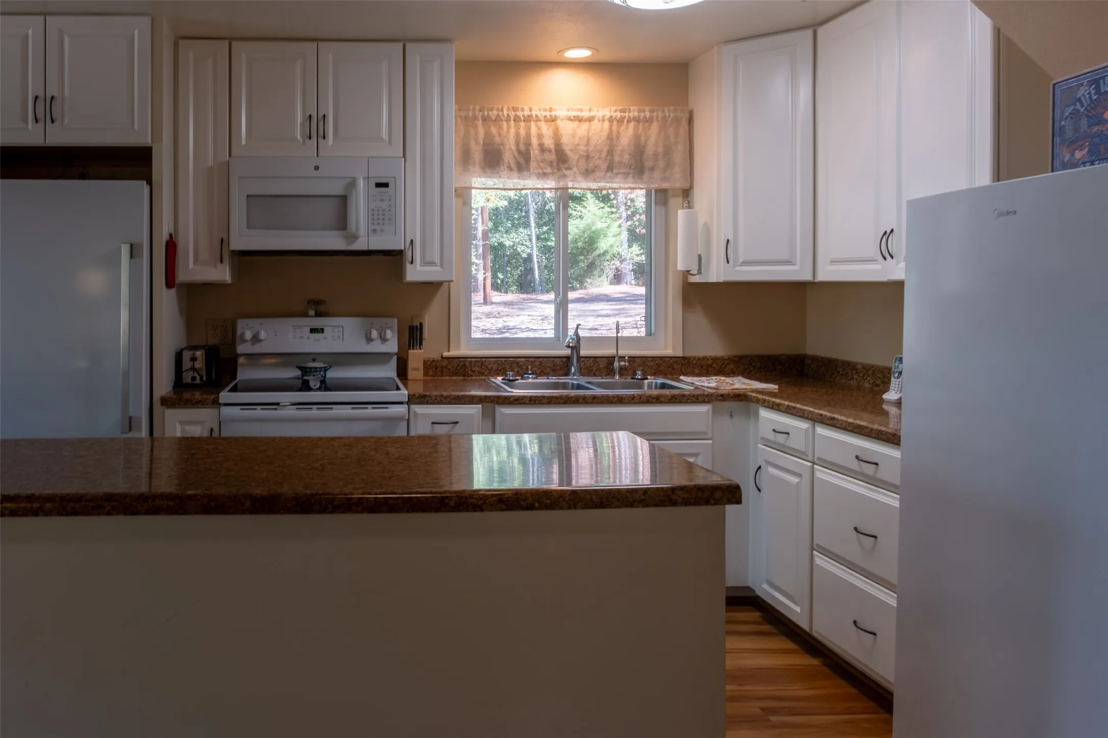 Kitchen featuring white cabinetry, granite-style countertops, wood-finish flooring, and a large window above the sink