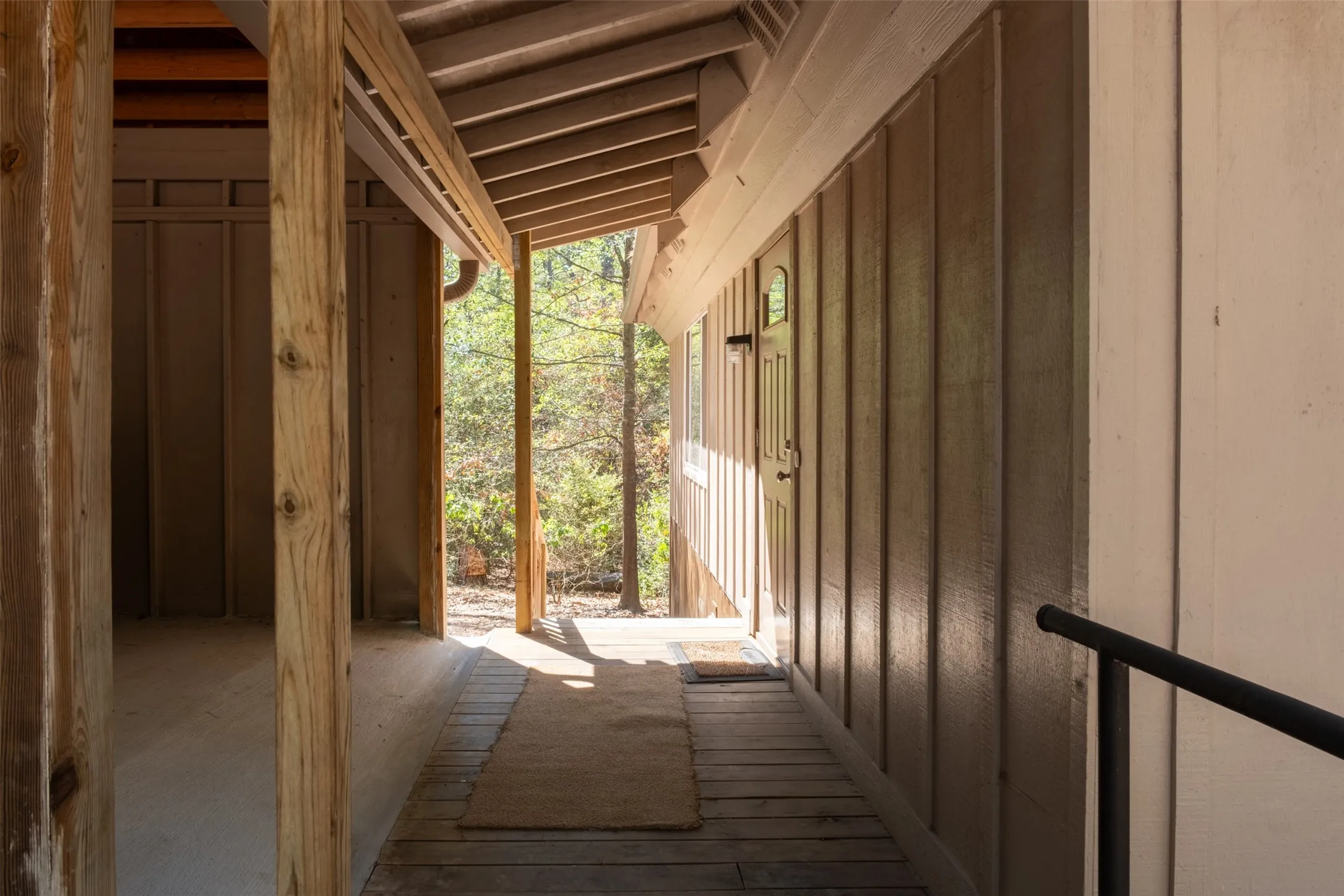 Covered exterior entry with wood-plank flooring, wood siding, and structural wood beams