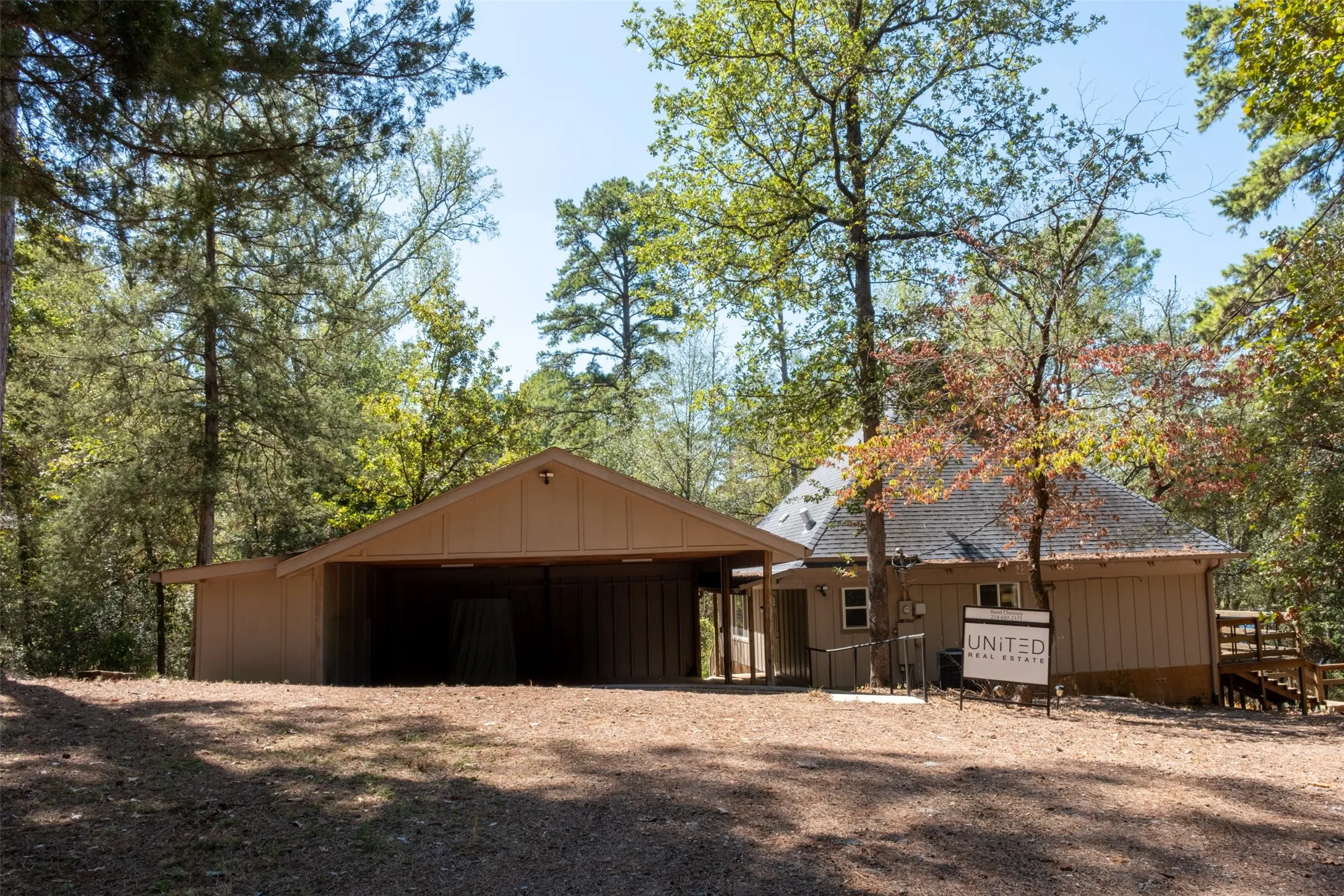 Wood-sided exterior structure with a covered parking area, a separate wood-sided building featuring a gable roof, and an exterior wood staircase