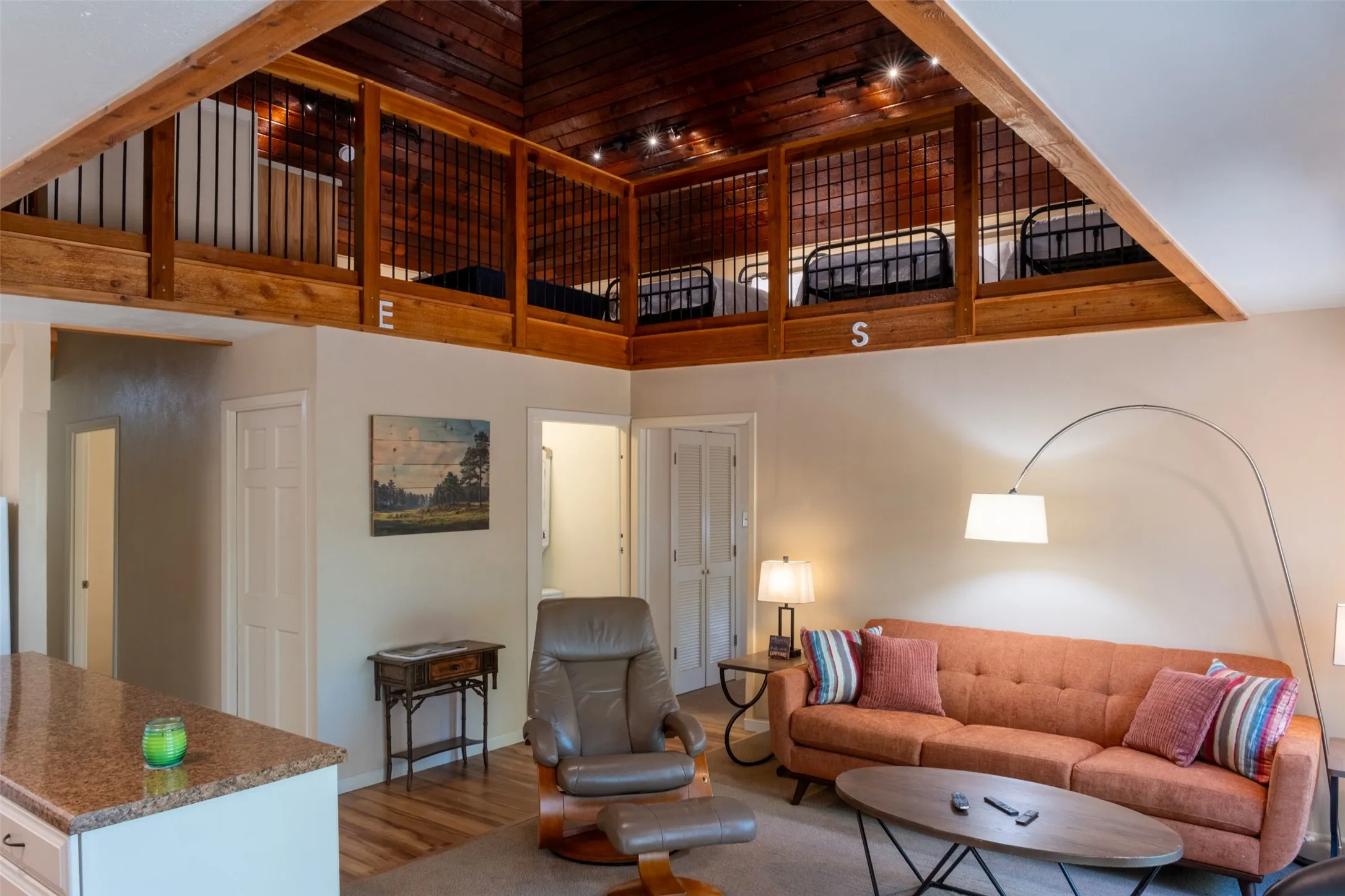 Vaulted wood-paneled ceiling with track lighting, exposed wood beams, and a wood-finish railing