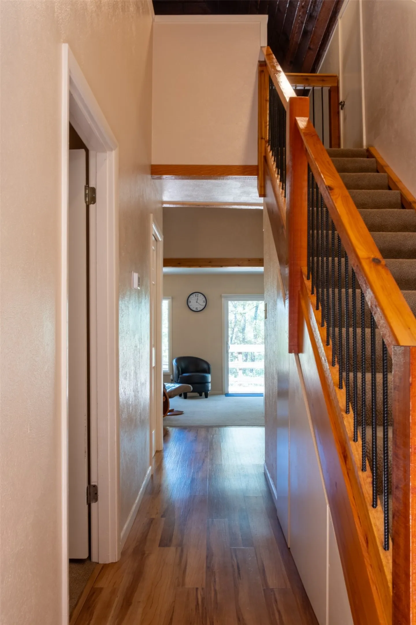 Wood-finish flooring, staircase with natural wood handrail and black metal balusters, exposed wood beam ceiling, and neutral wall tones