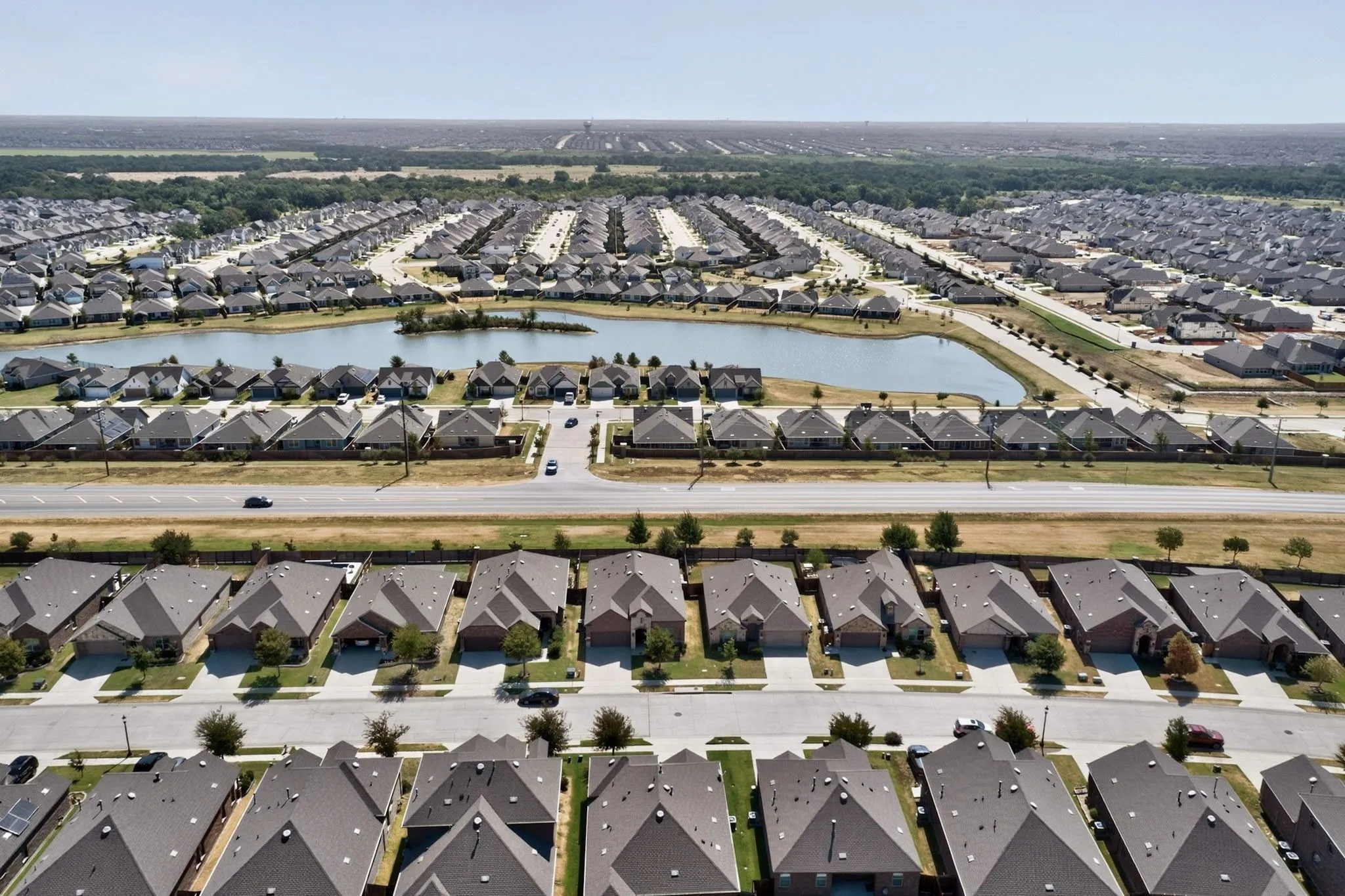 Expansive residential development featuring numerous single-family homes, a central community pond, and wide roadways