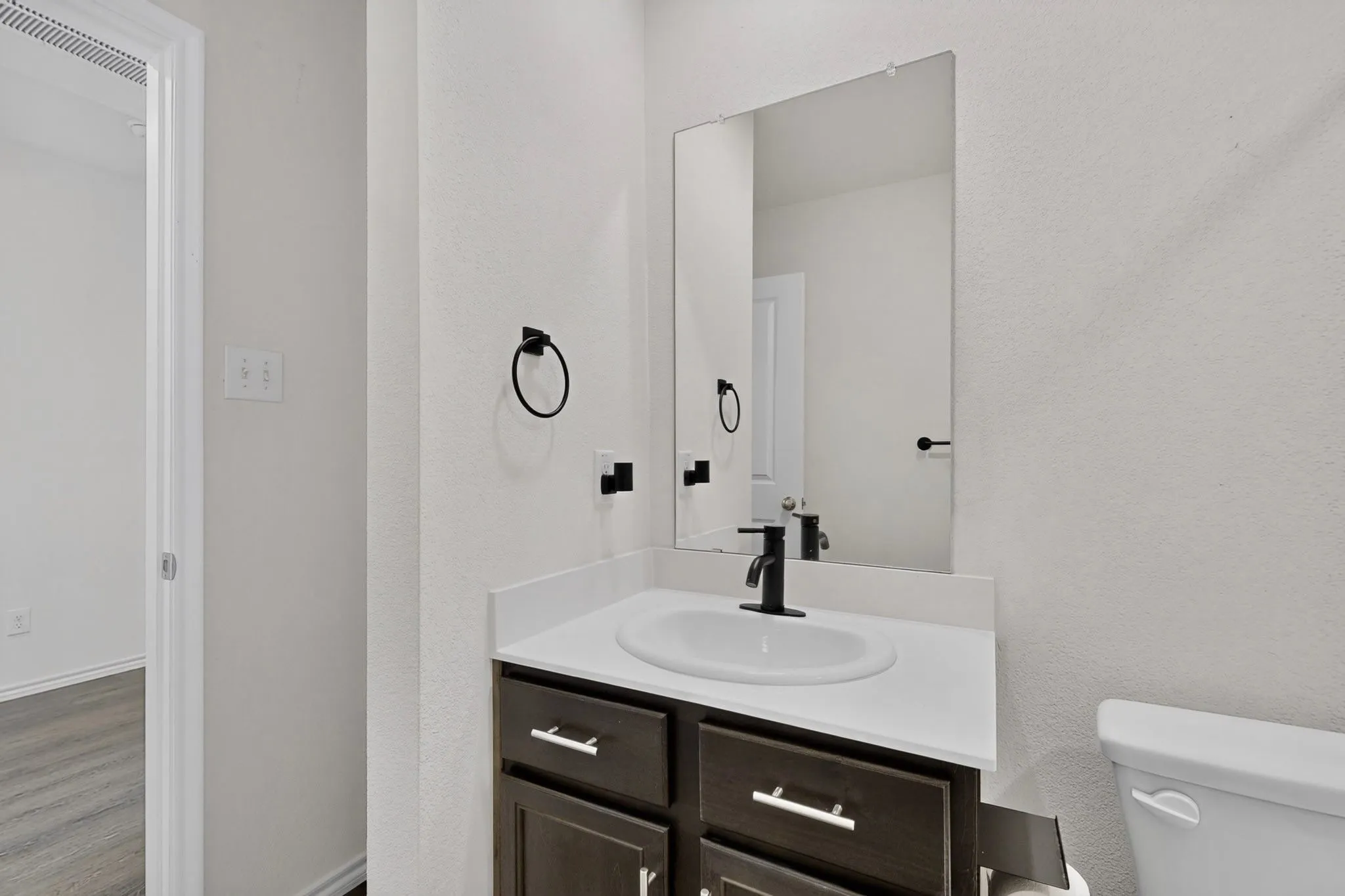 Vanity with dark wood cabinetry, white countertop, and an undermount sink with a matte black faucet