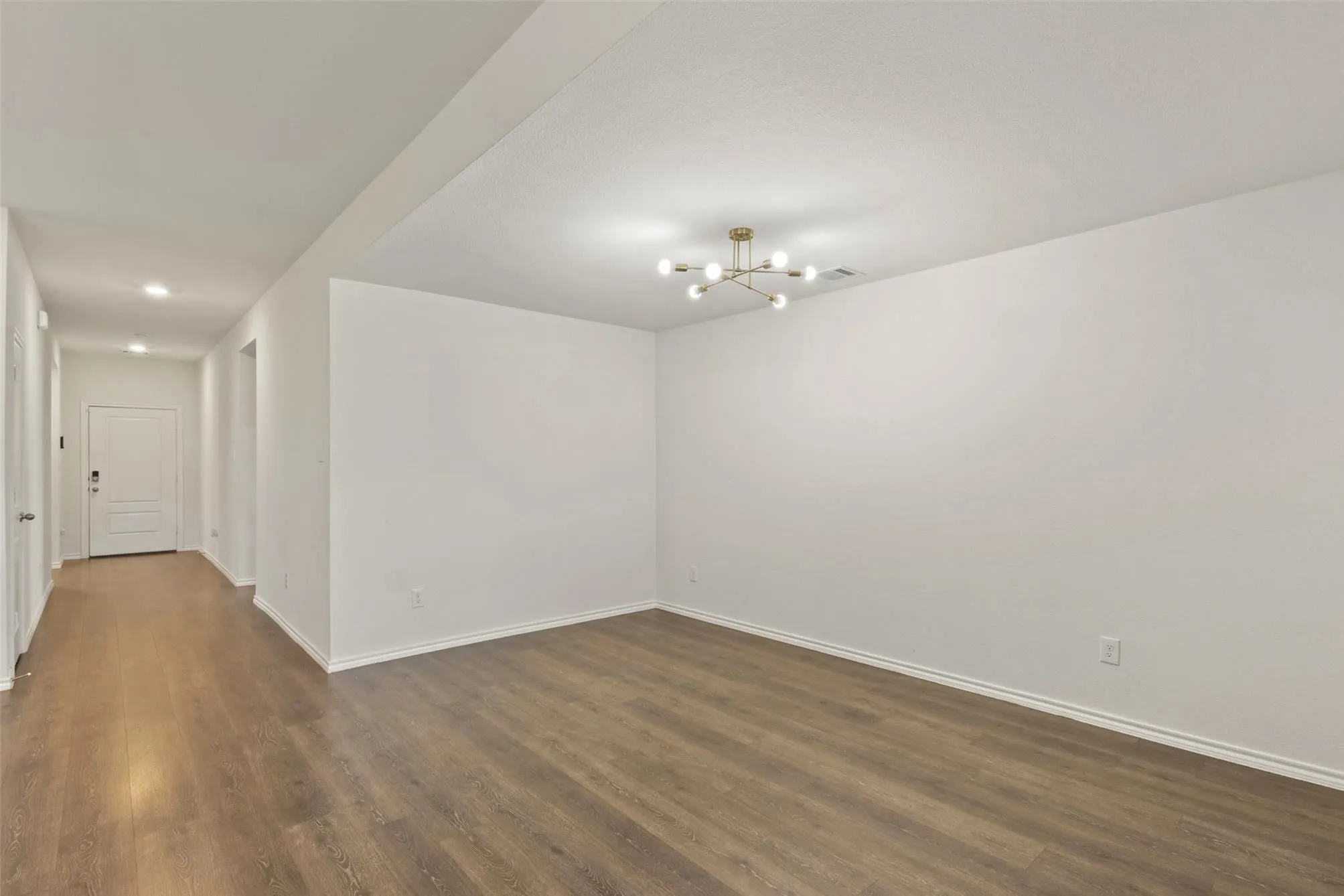 Spacious interior with wood-finish flooring, a modern brass chandelier, and recessed lighting in the hallway
