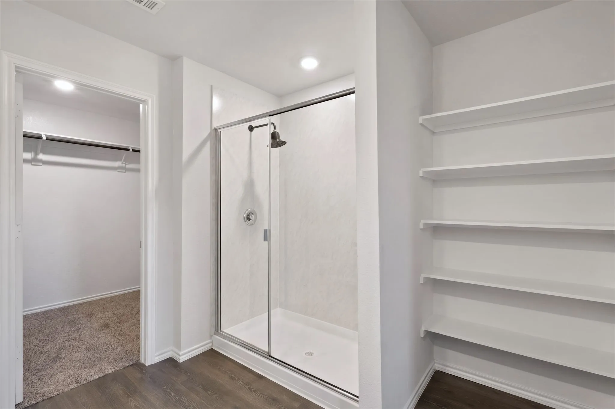 Glass-enclosed shower with a dark bronze showerhead, wood-finish flooring, recessed lighting, and built-in shelving