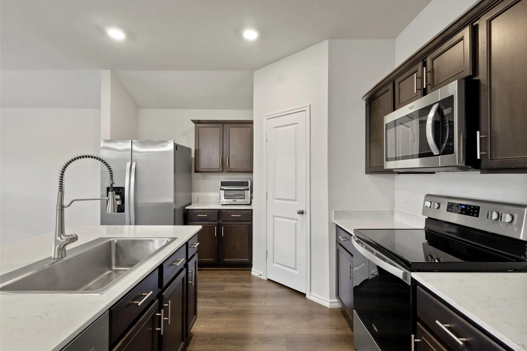 Modern kitchen featuring stainless steel appliances, dark wood-finish cabinetry, light stone-finish countertops, and wood-finish flooring