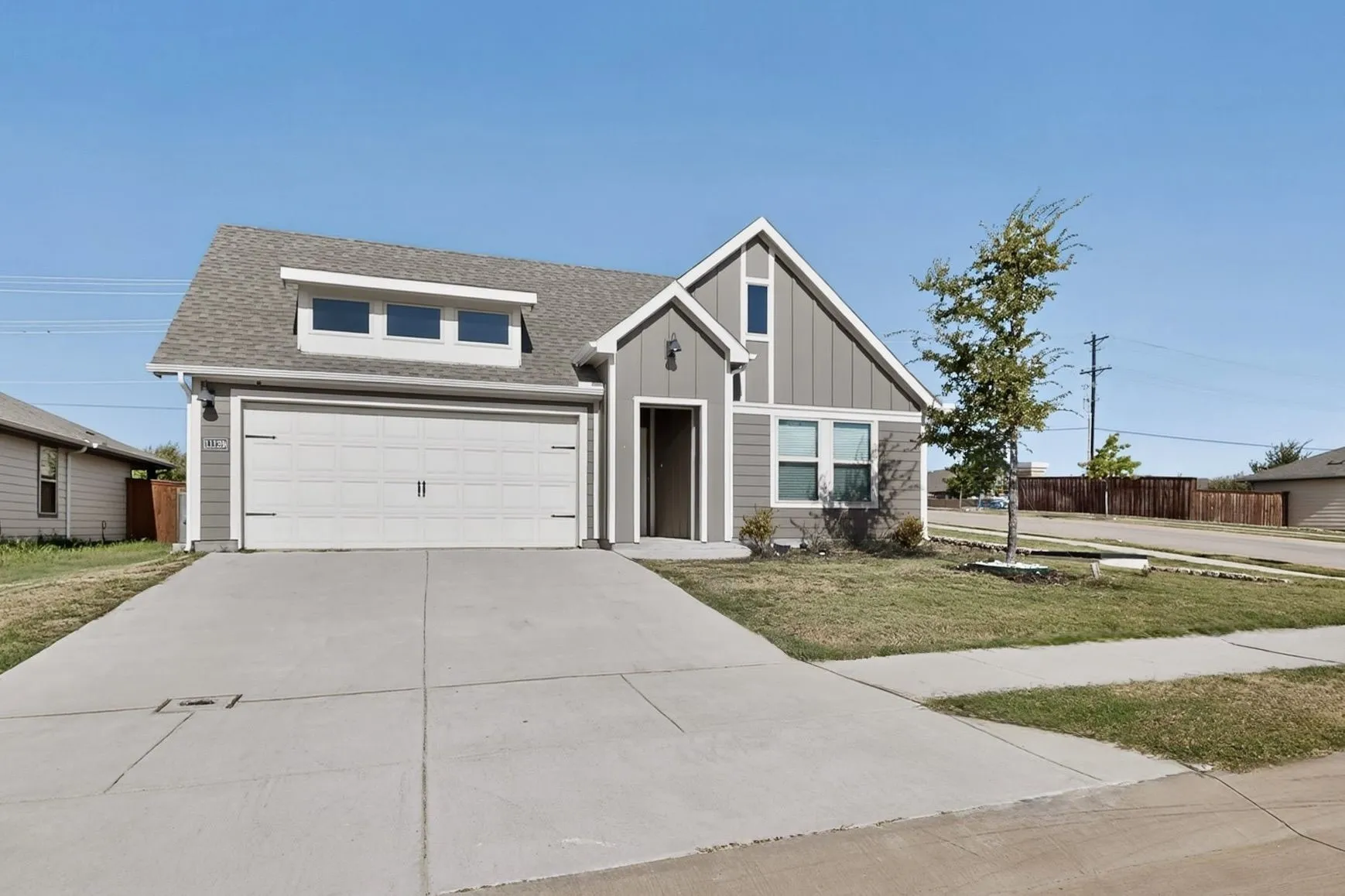 Contemporary exterior featuring a dormer window, an attached garage, a mature tree, and a concrete driveway