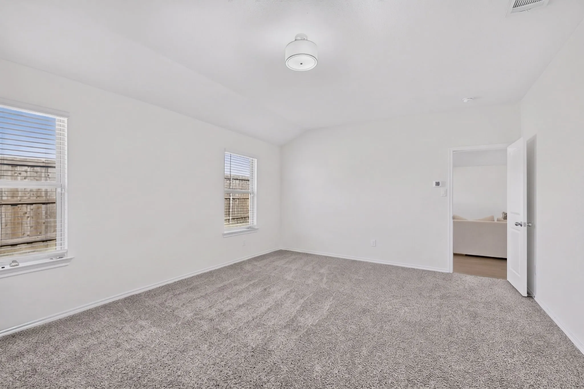 Neutral gray carpeting, white painted walls, two windows with blinds, and a white ceiling light fixture