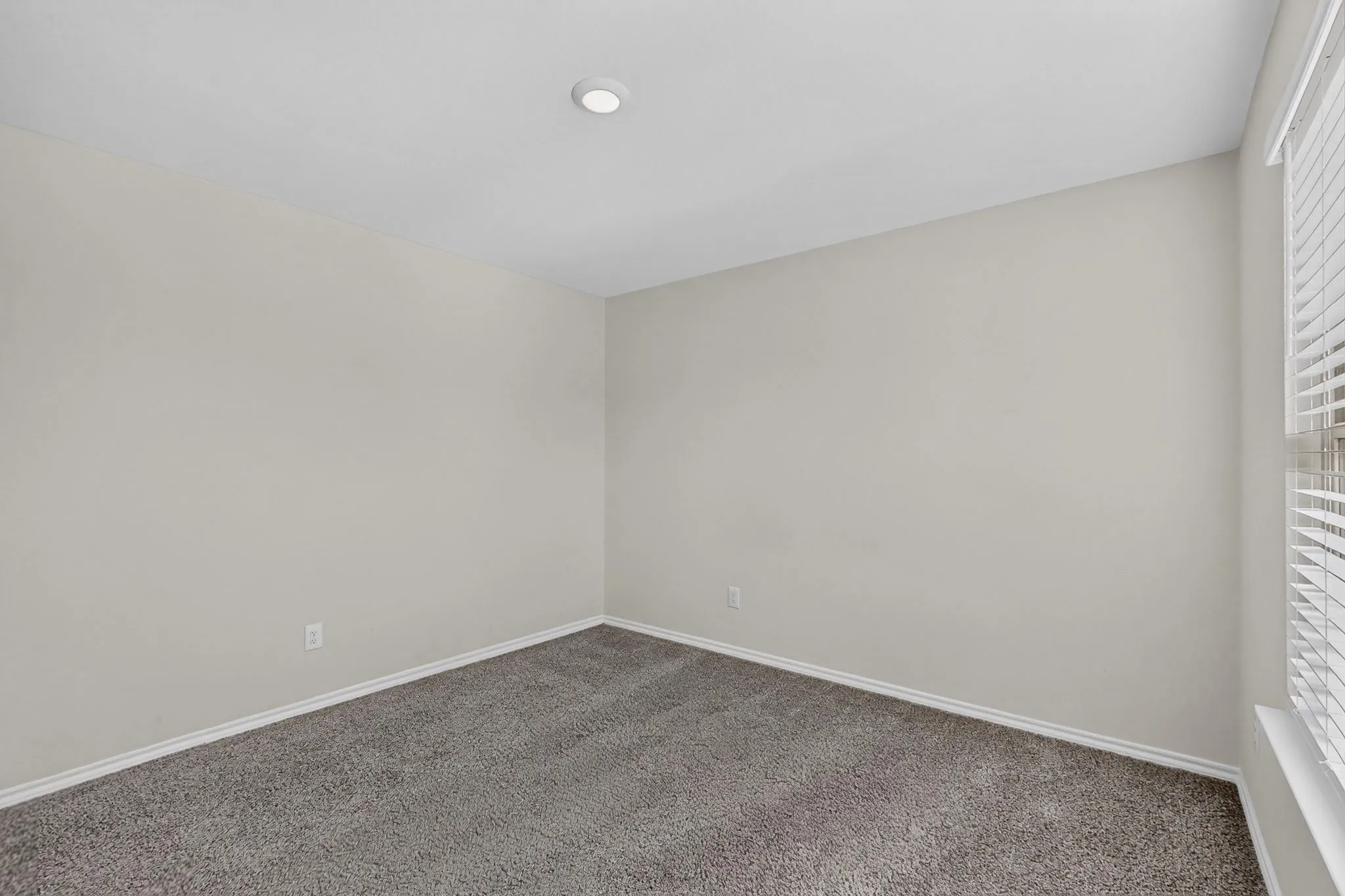 Neutral wall tones with gray carpeting, recessed lighting, and a window with blinds