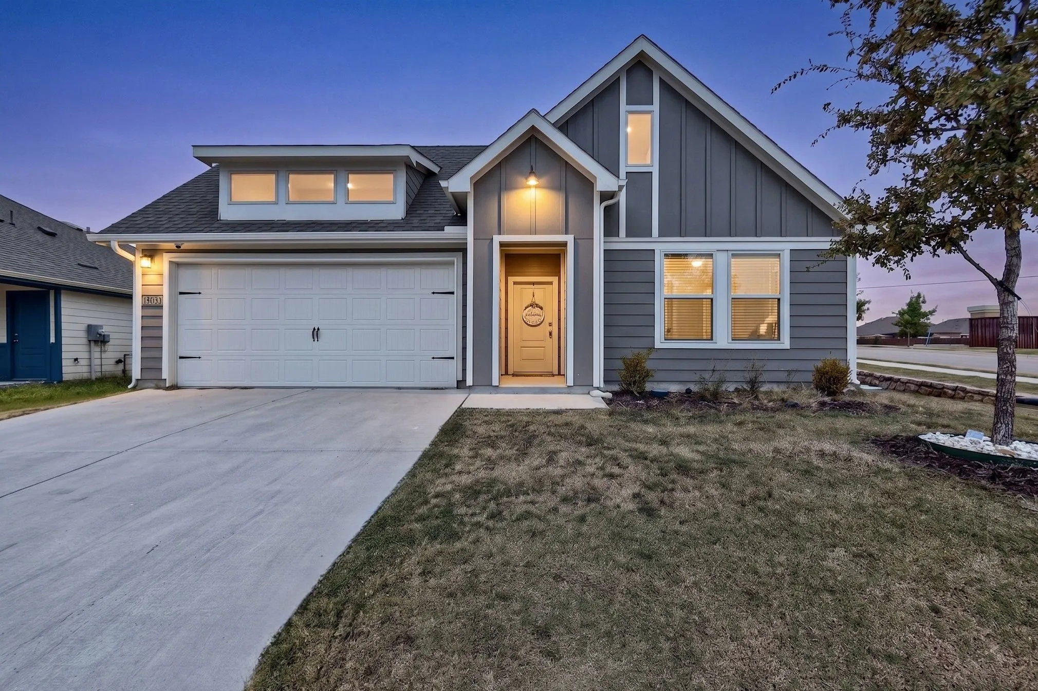 Modern façade with mixed siding, attached two-car garage, concrete driveway, front porch entry, and established landscaping