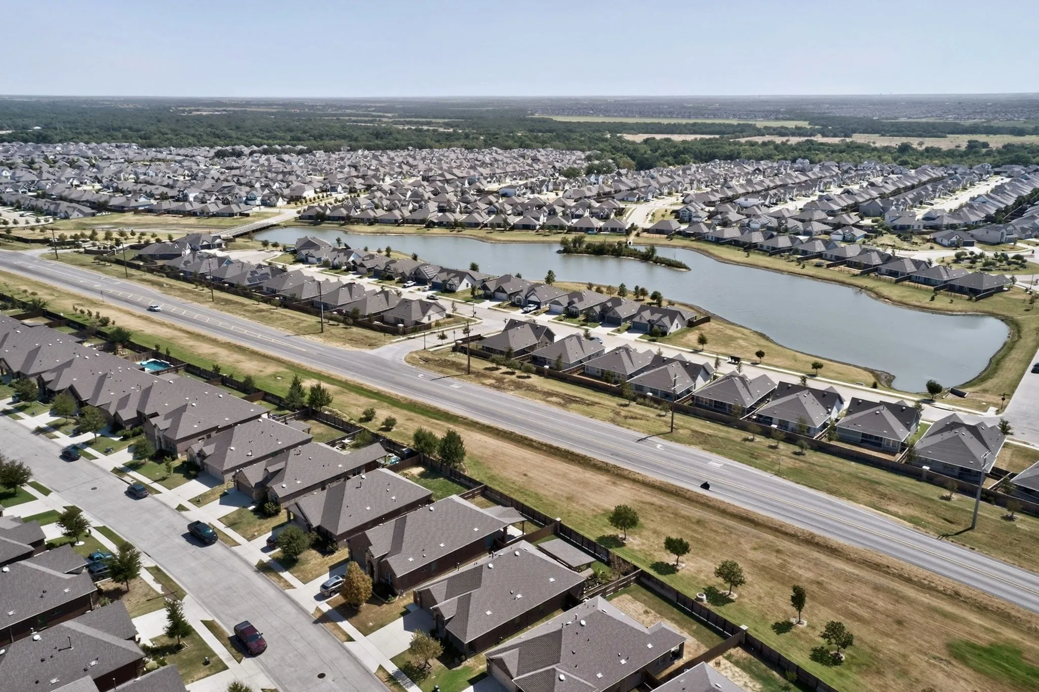 Expansive residential development featuring numerous single-family homes, a central body of water, and surrounding green spaces