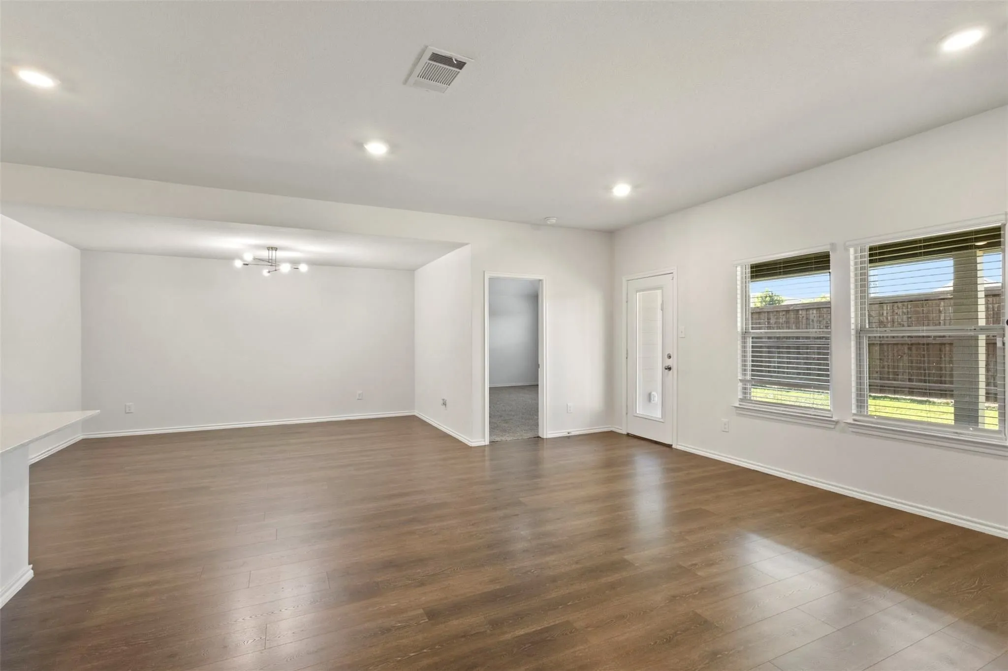 Spacious room featuring wood-finish flooring, recessed lighting, multiple windows, and a ceiling-mounted light fixture