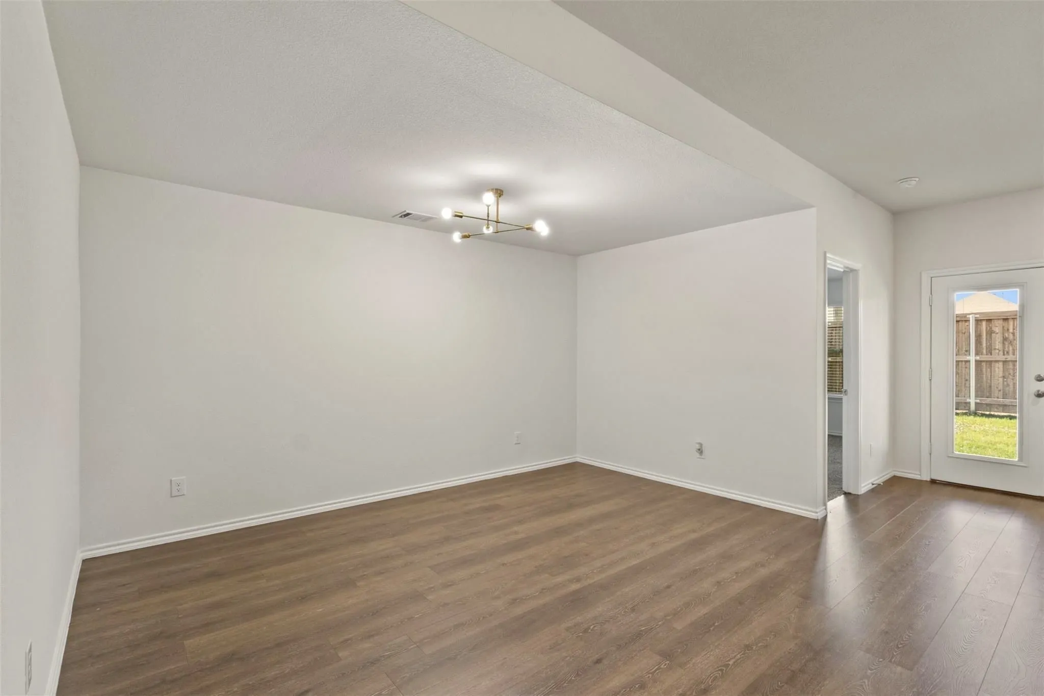Spacious room with wood-finish flooring, contemporary ceiling light fixture, and a rear exterior door with a glass panel