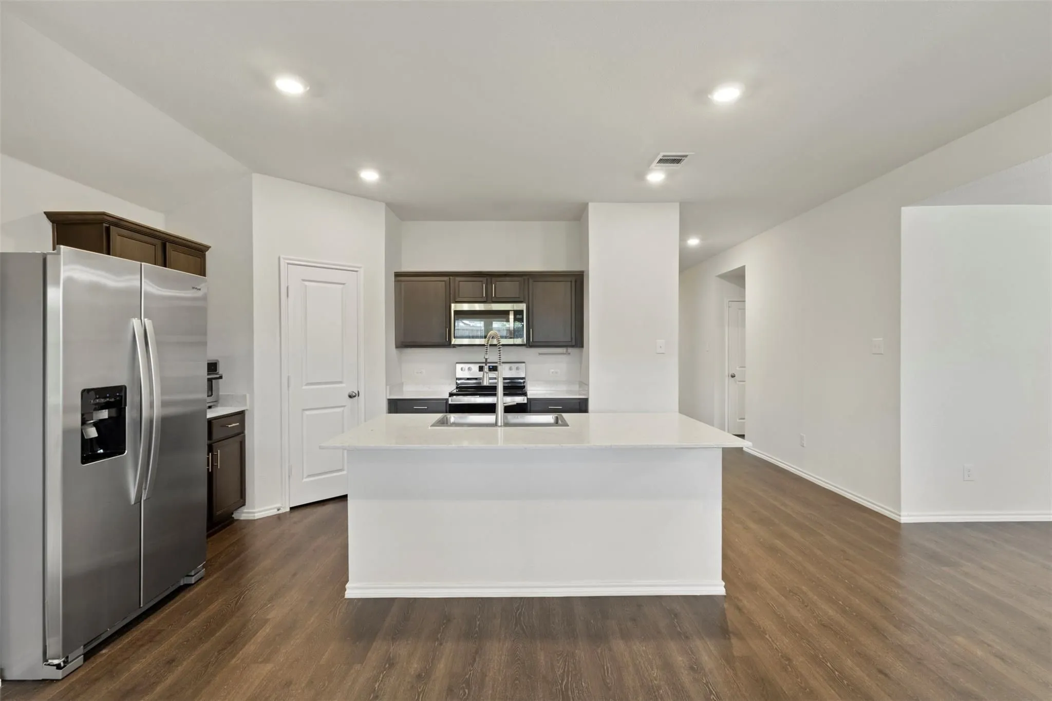 Kitchen featuring dark wood-finish cabinetry, stainless steel appliances, a white tile backsplash, a large center island with an undermount sink, and wood-finish flooring